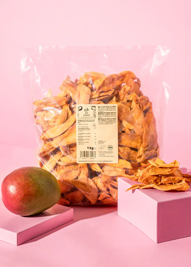 un sac de mangue séchée est assis sur une table rose à côté d' une mangue