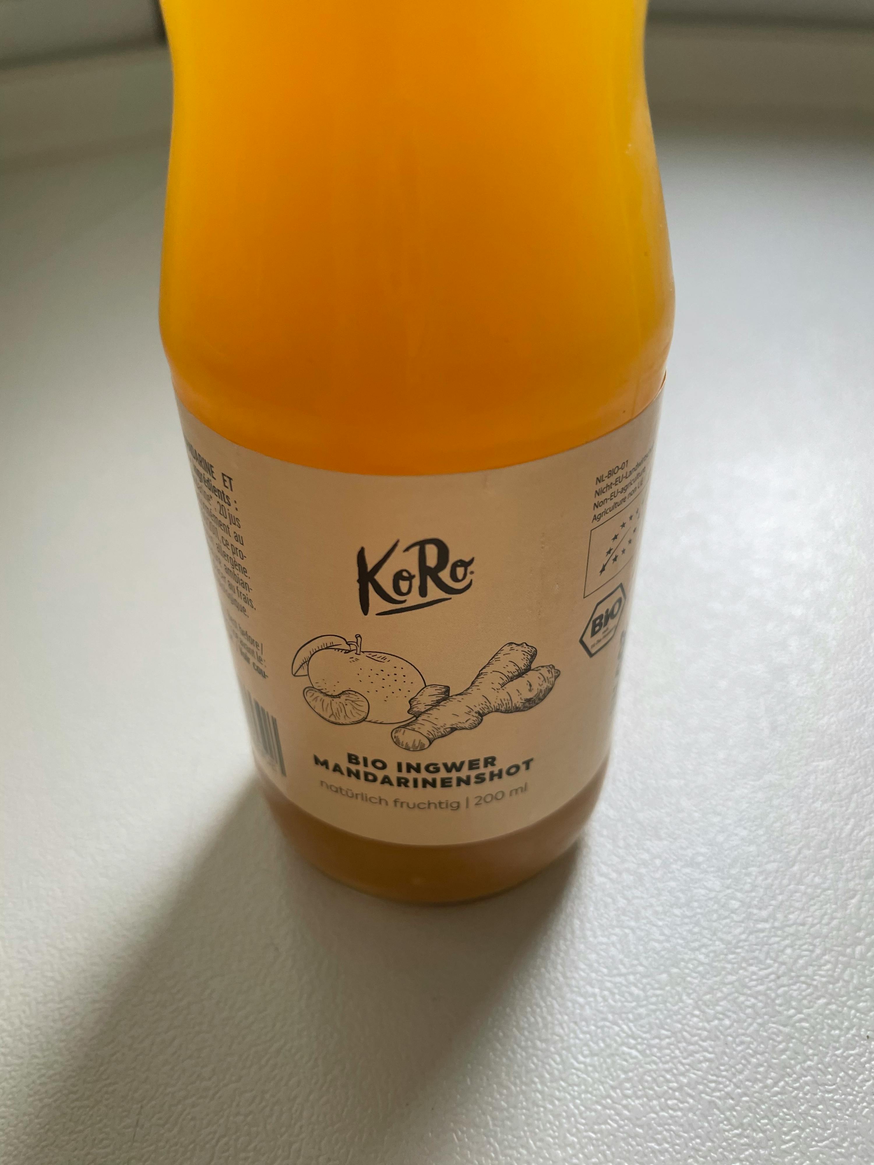 une bouteille de jus de mandarine et de gingembre est posée sur une surface blanche