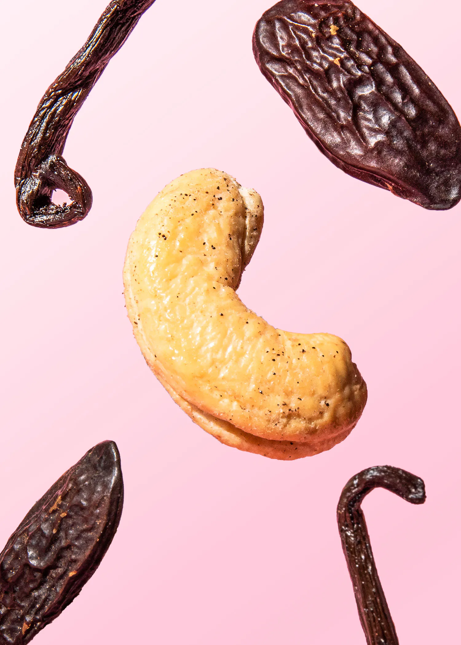 a cashew nut is surrounded by vanilla pods on a pink background