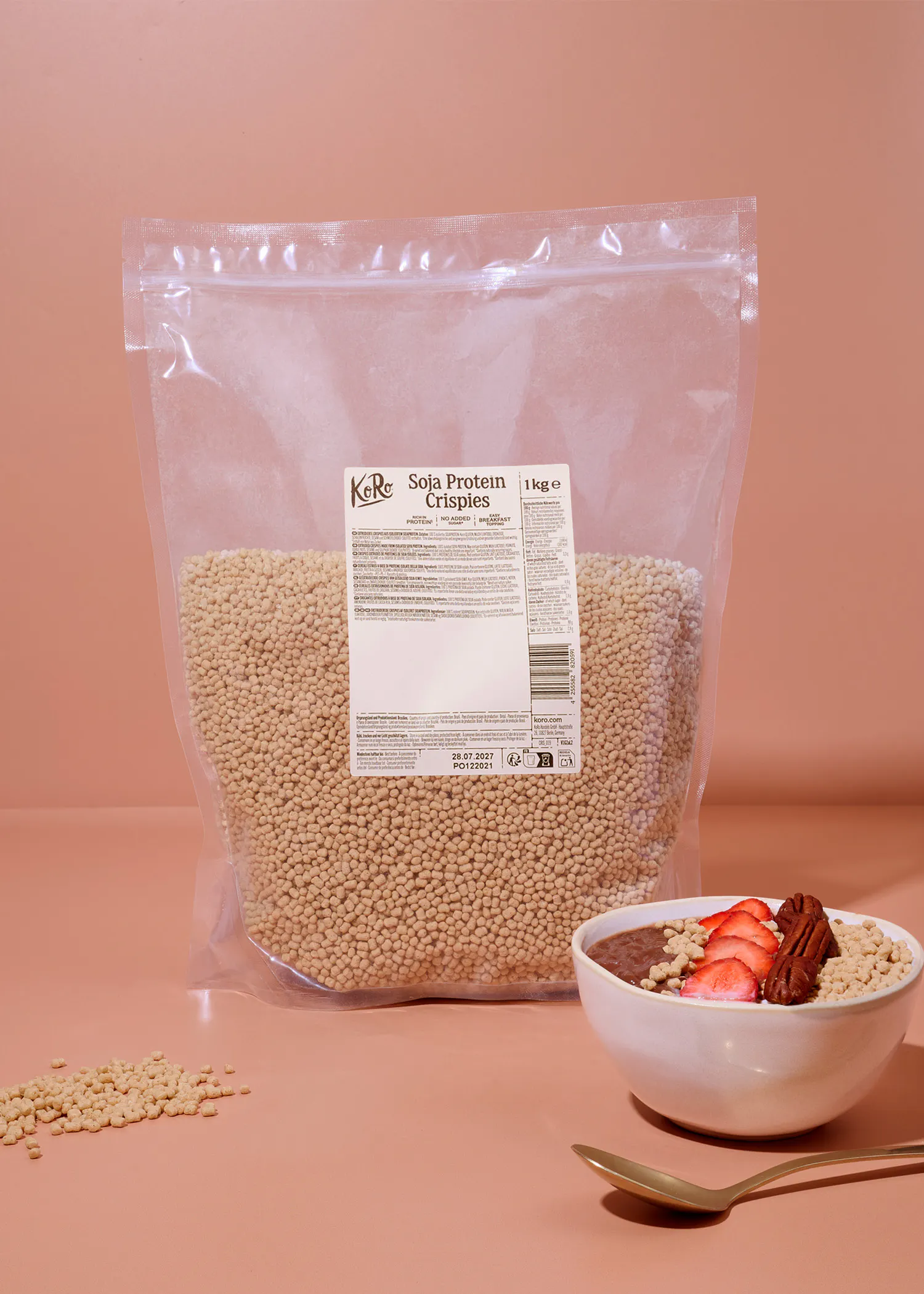 un sachet d'un kilogramme de pépites de protéines de soja koro posé à côté d'un bol de petit-déjeuner contenant du chocolat, des fraises, des noix de pécan et des pépites de soja.