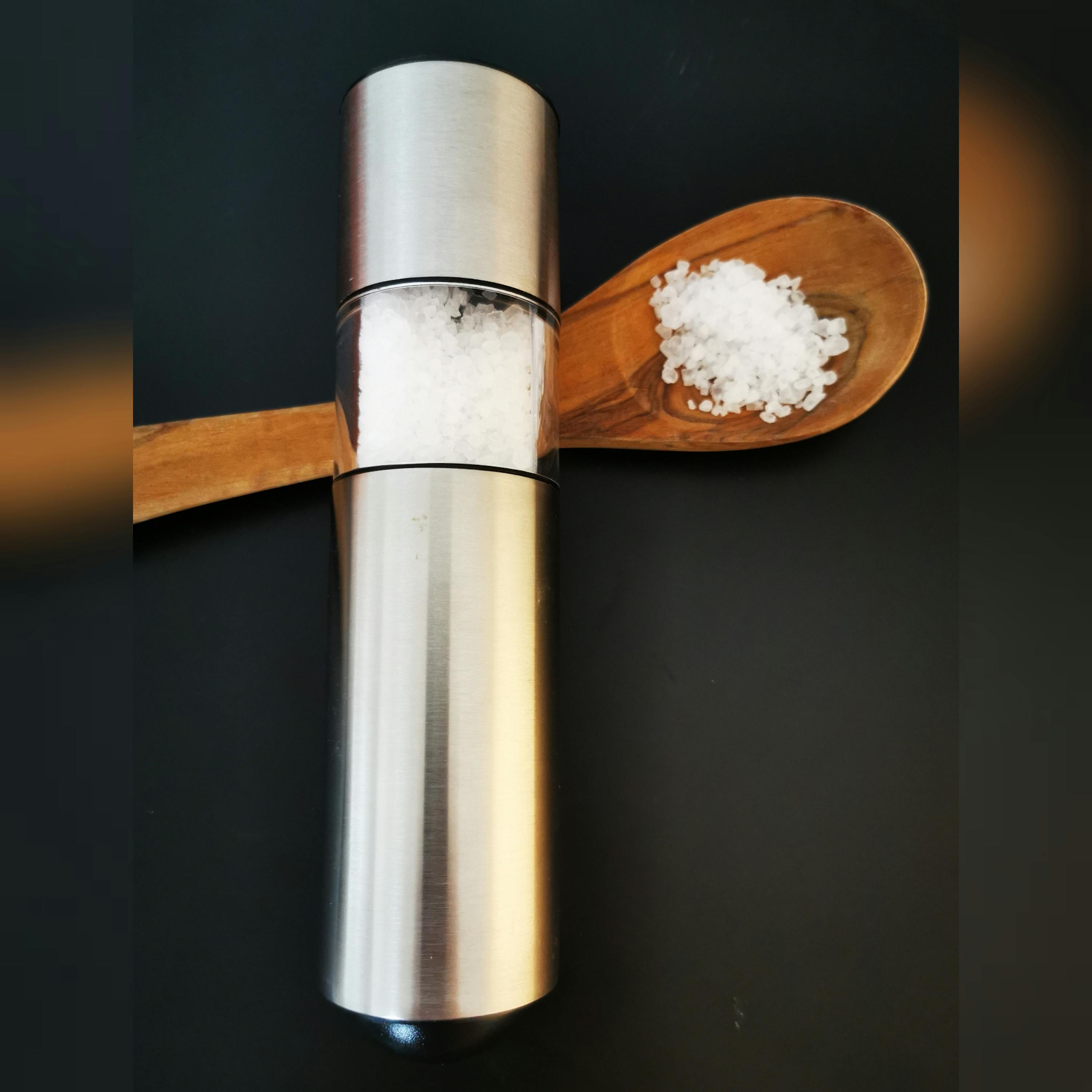 eine Salzmühle steht neben einem Holzlöffel mit Salz darin
