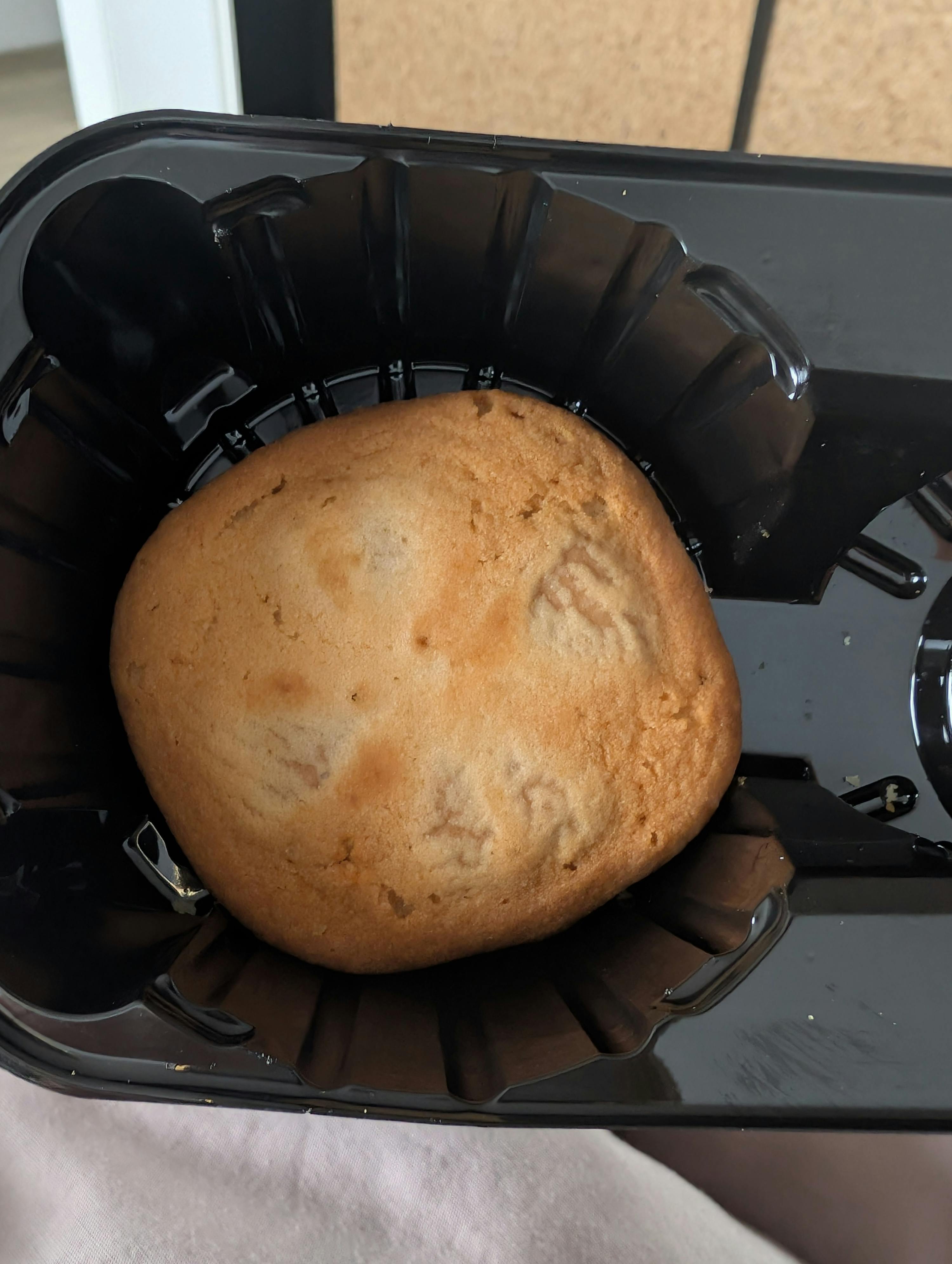 ein rundes, hellbraunes gebäckstück in einer schwarzen plastikschale.