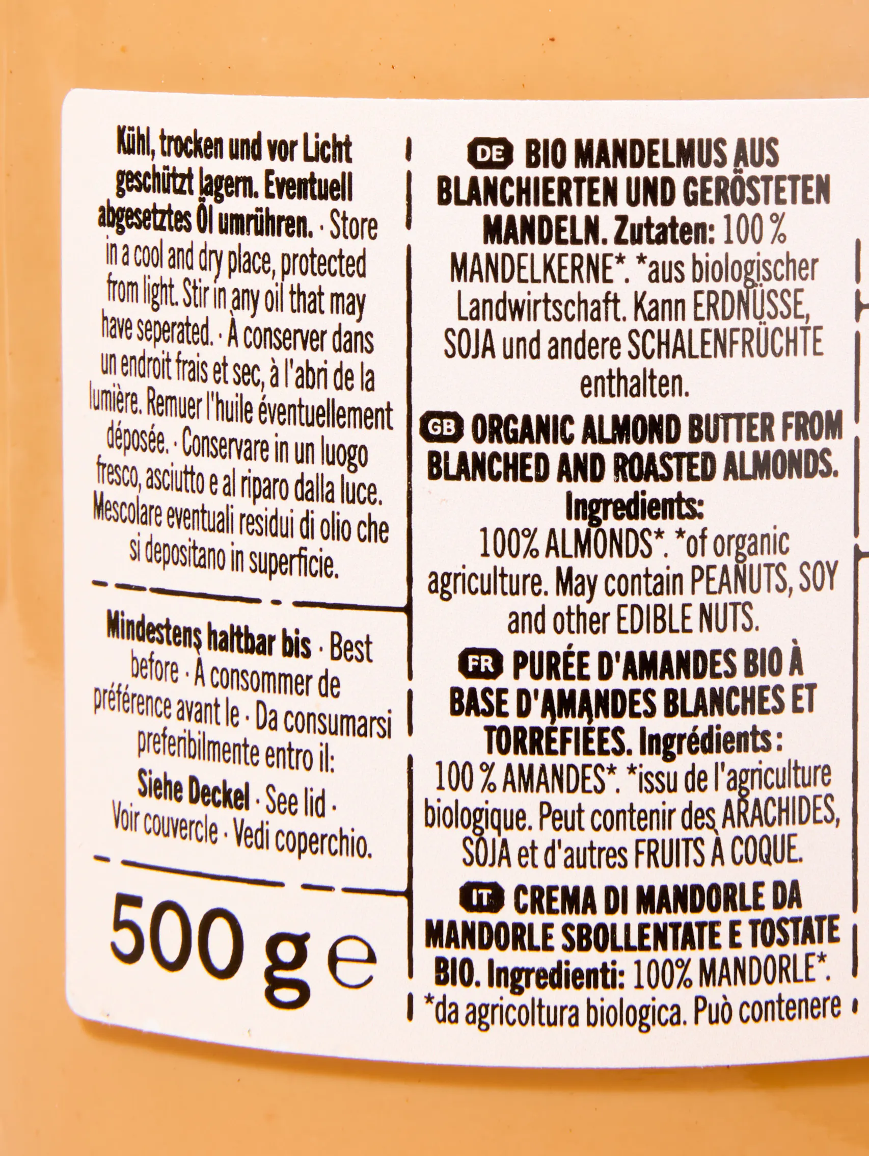 etikett eines glases mit bio-mandelmus, das zutaten, lagerhinweise und das mindesthaltbarkeitsdatum in mehreren sprachen auflistet.
