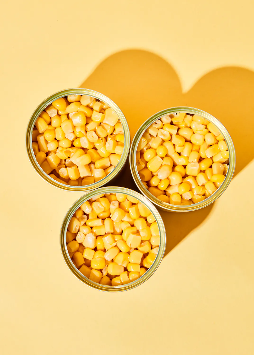 three cans of corn are sitting on a yellow surface