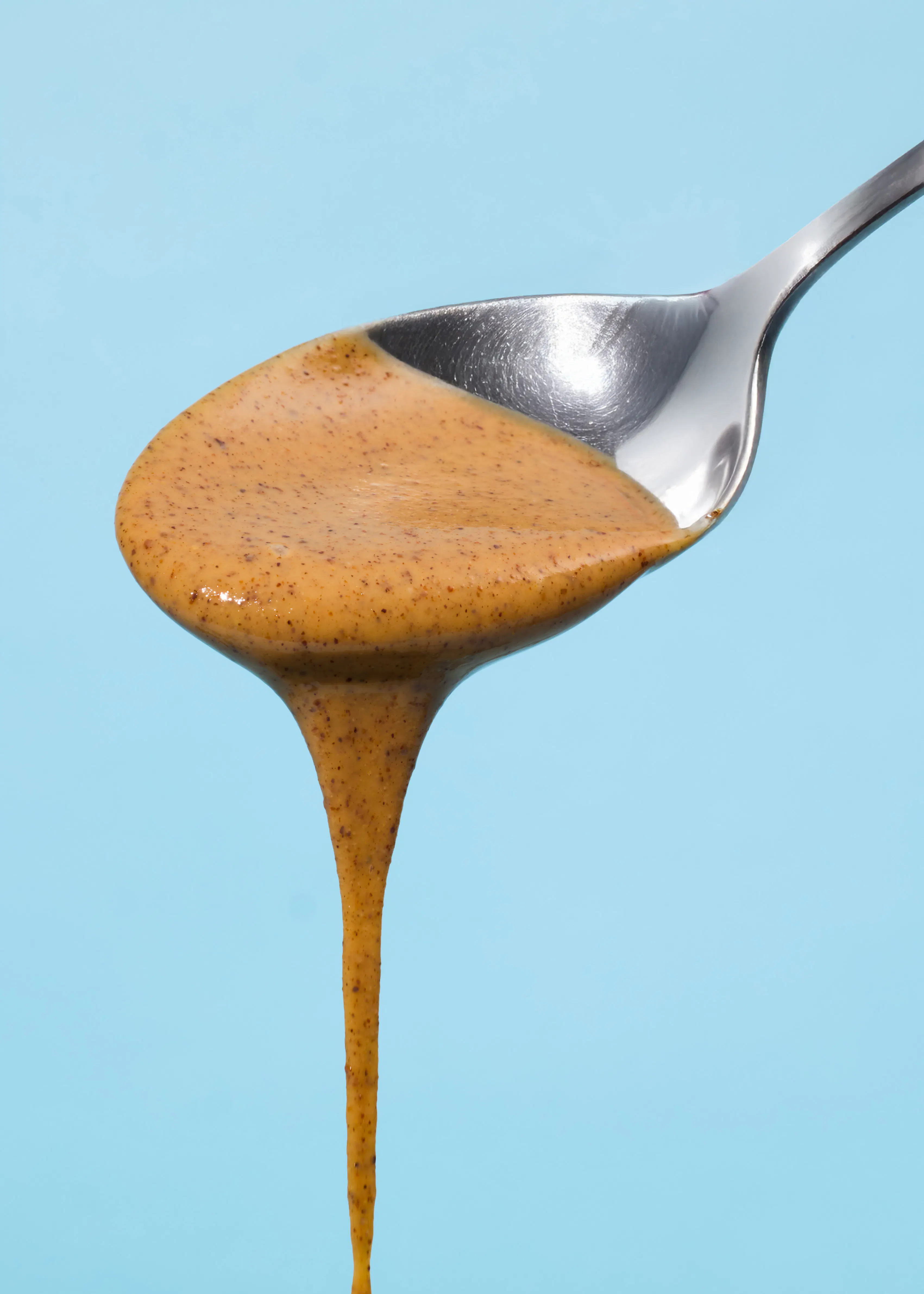 une cuillère remplie de sauce brune sur fond bleu