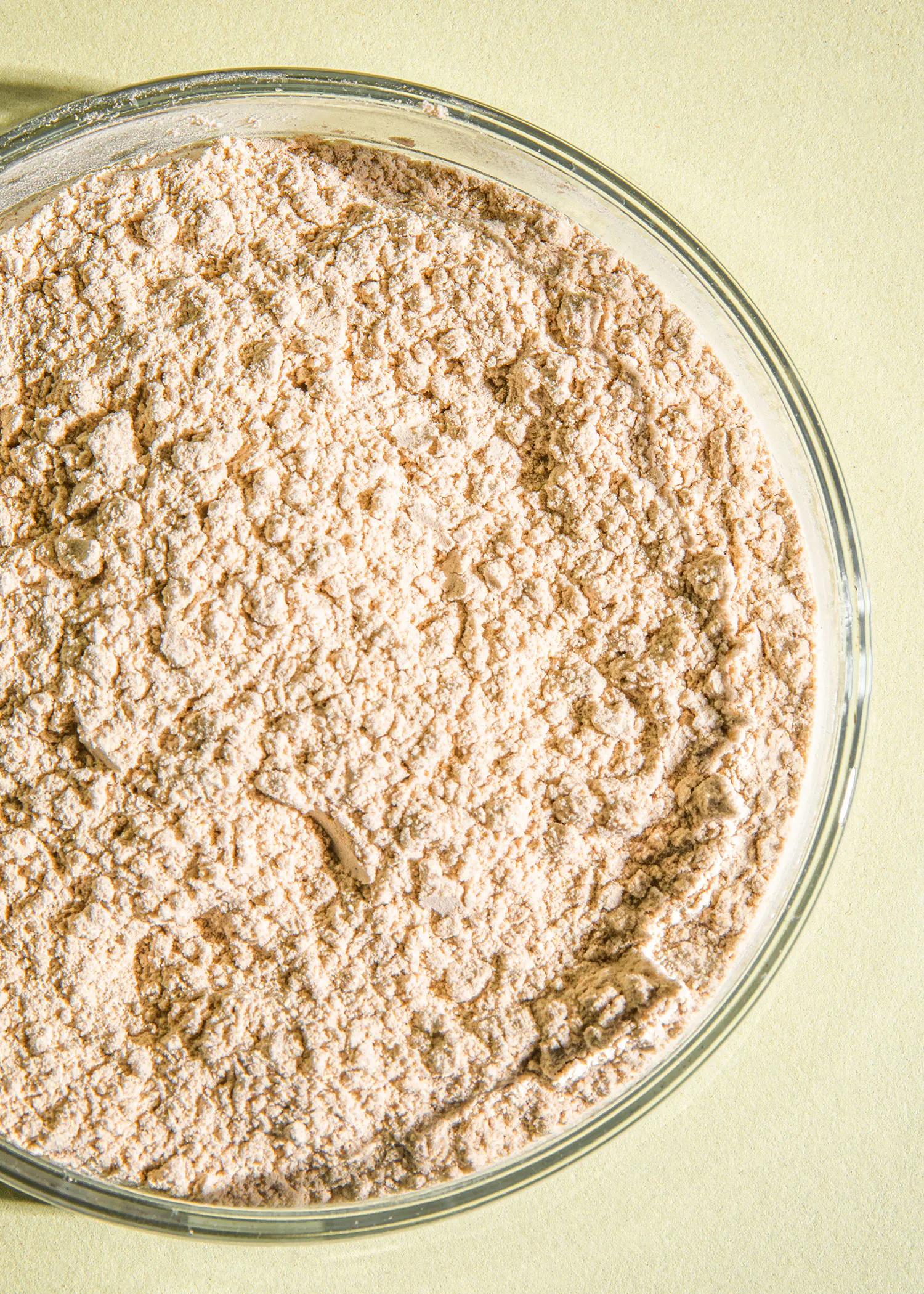 a glass bowl filled with brown powder on a yellow surface
