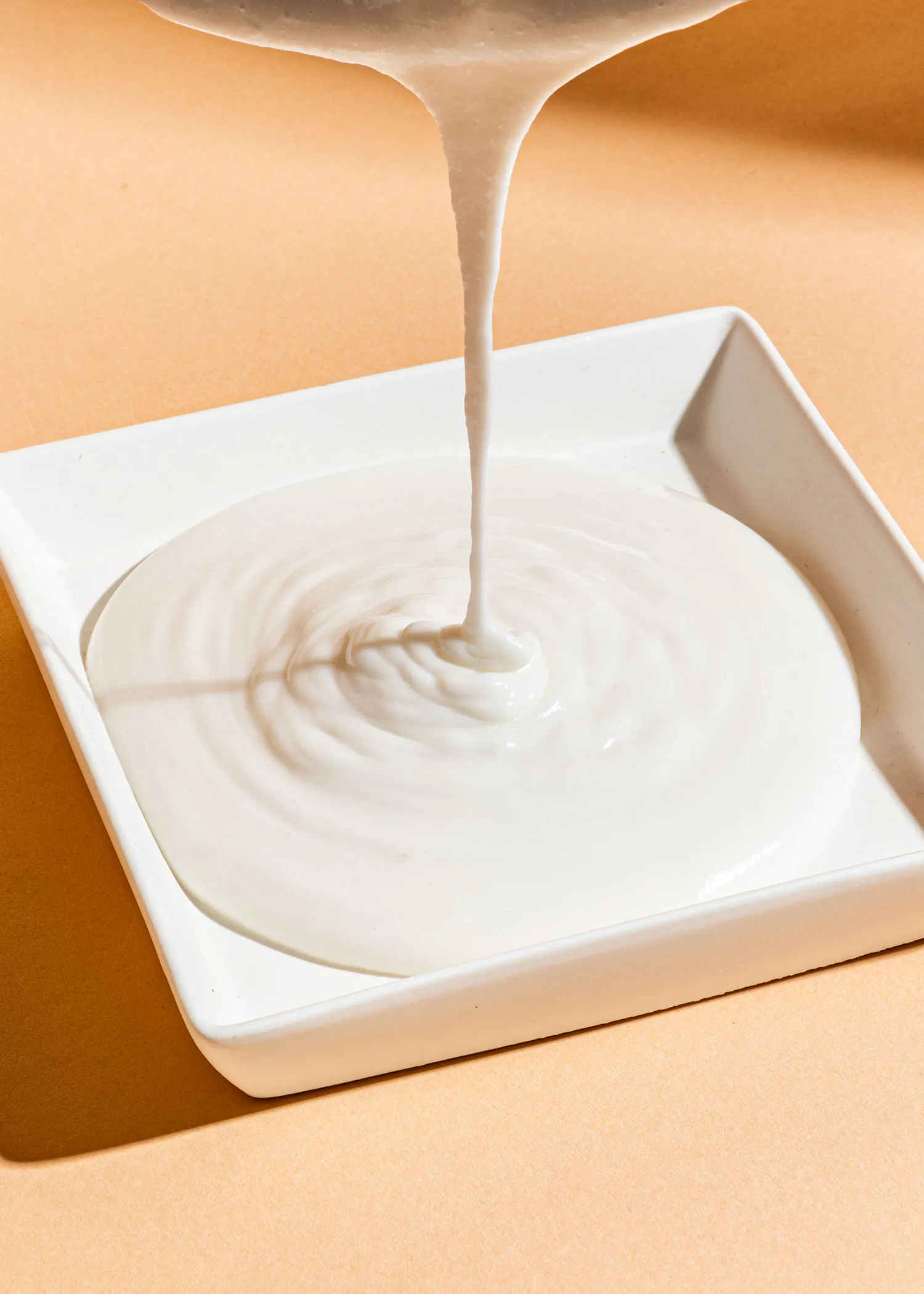 une sauce blanche est versée sur une assiette carrée