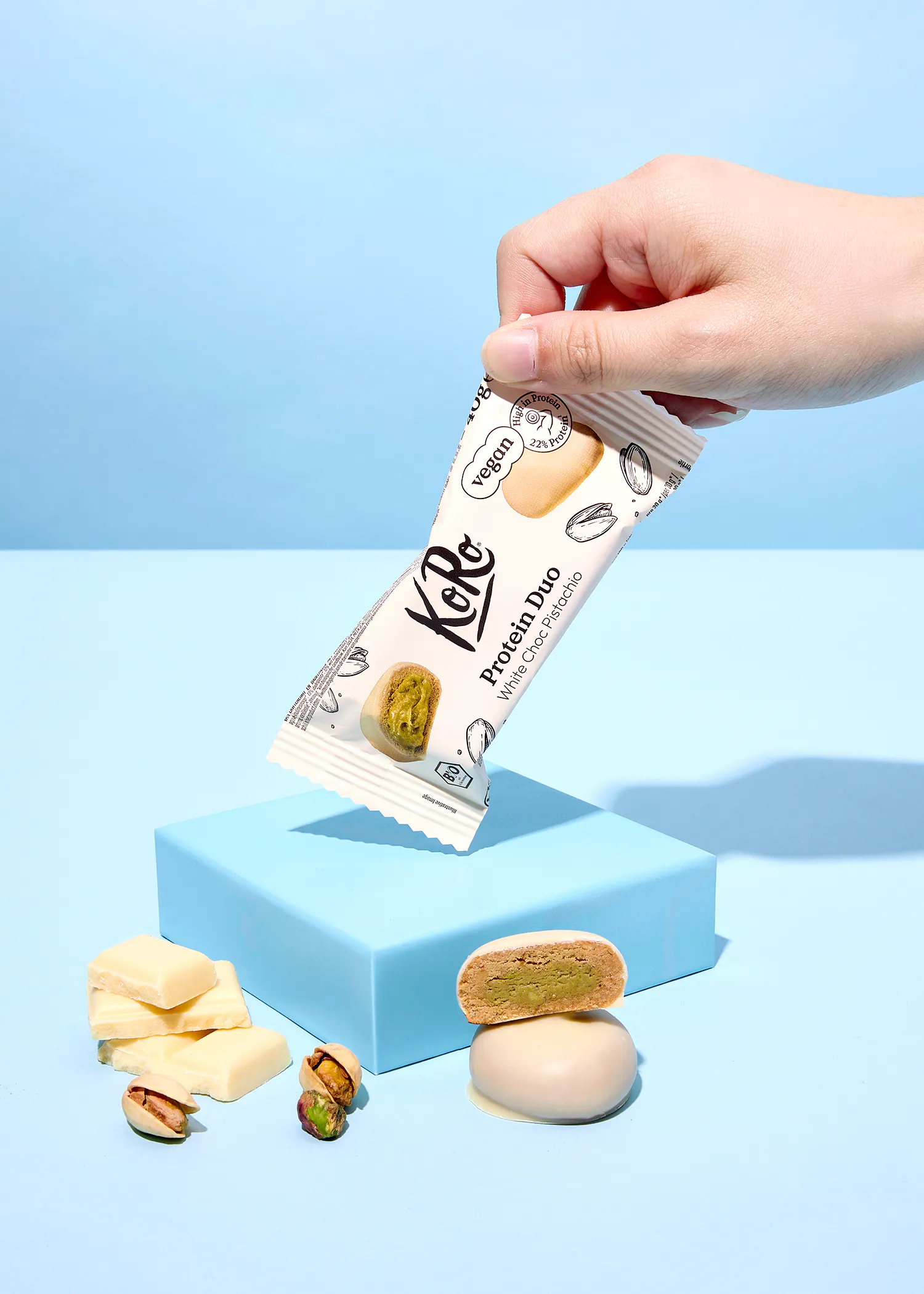 une personne tient une barre de protéines avec des pistaches et du chocolat blanc