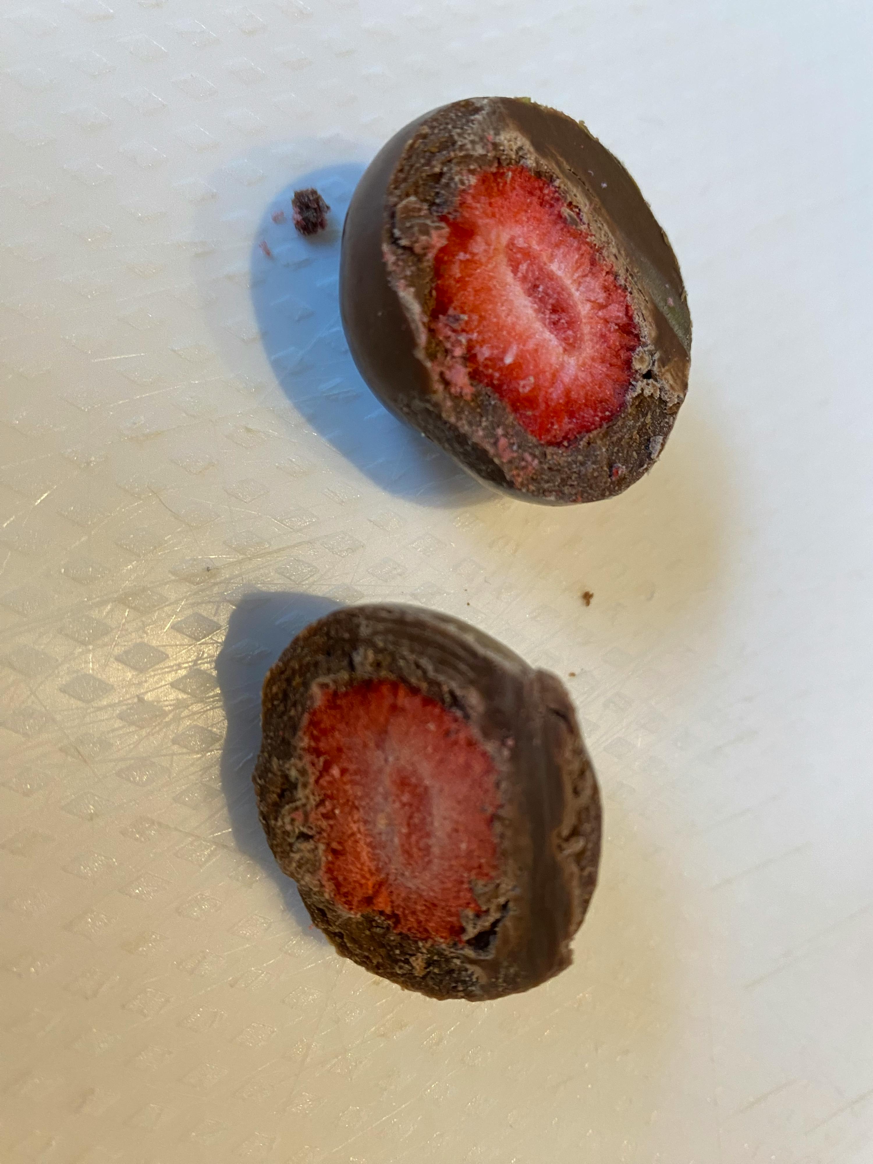 a chocolate covered strawberry is cut in half on a white surface