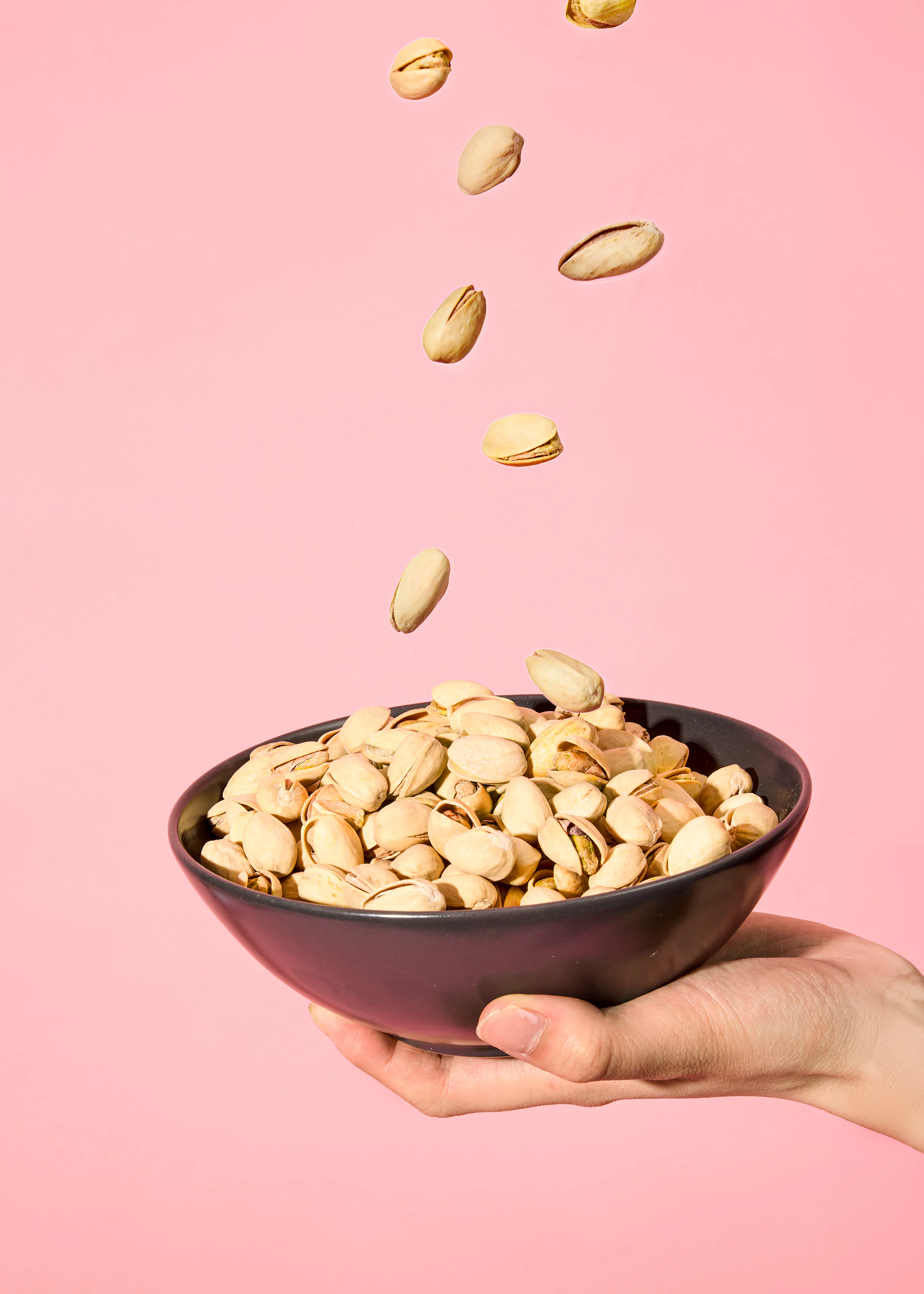 une main tient un bol de pistaches qui tombent dessus