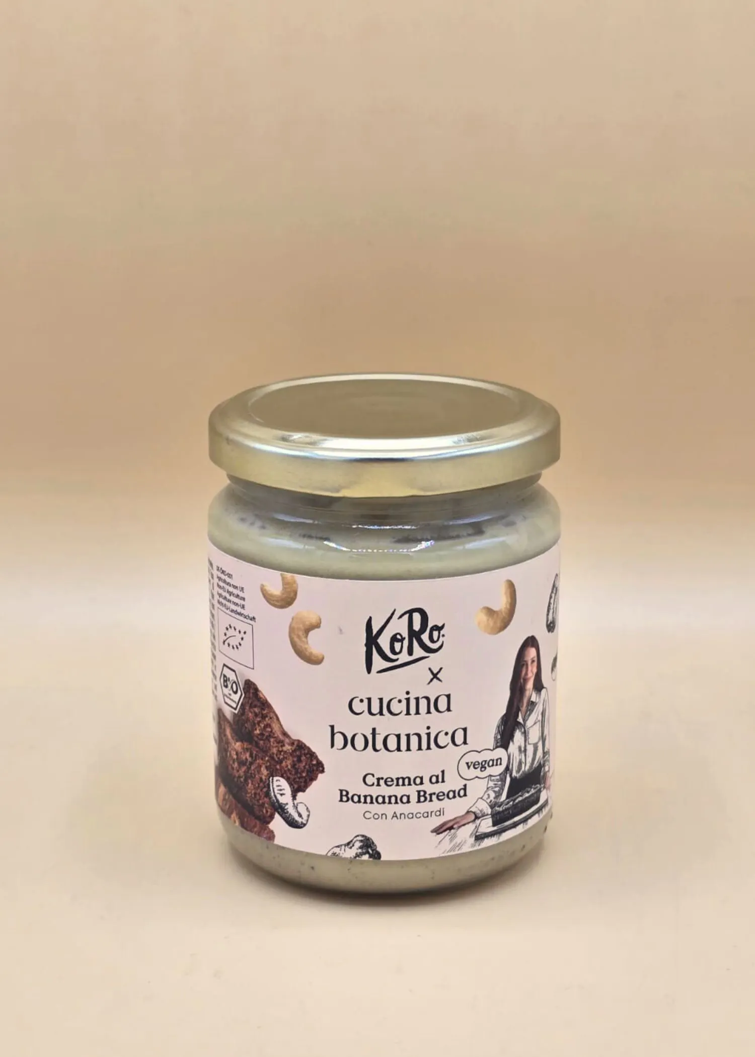 un barattolo di crema spalmabile vegana koro cucina botanica al banana bread con anacardi, con etichetta bianca e tappo dorato, su sfondo chiaro.