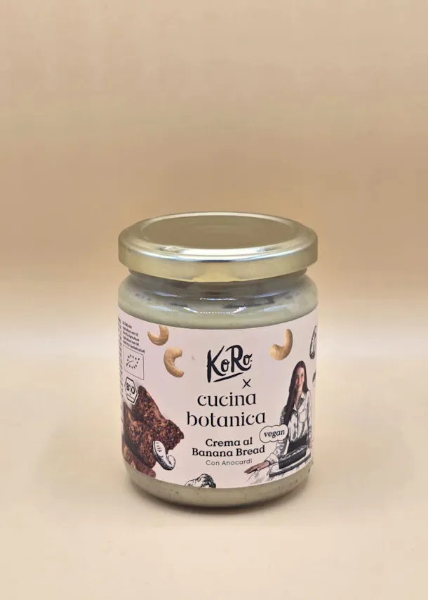 un barattolo di crema spalmabile vegana koro cucina botanica al banana bread con anacardi, con etichetta bianca e tappo dorato, su sfondo chiaro.
