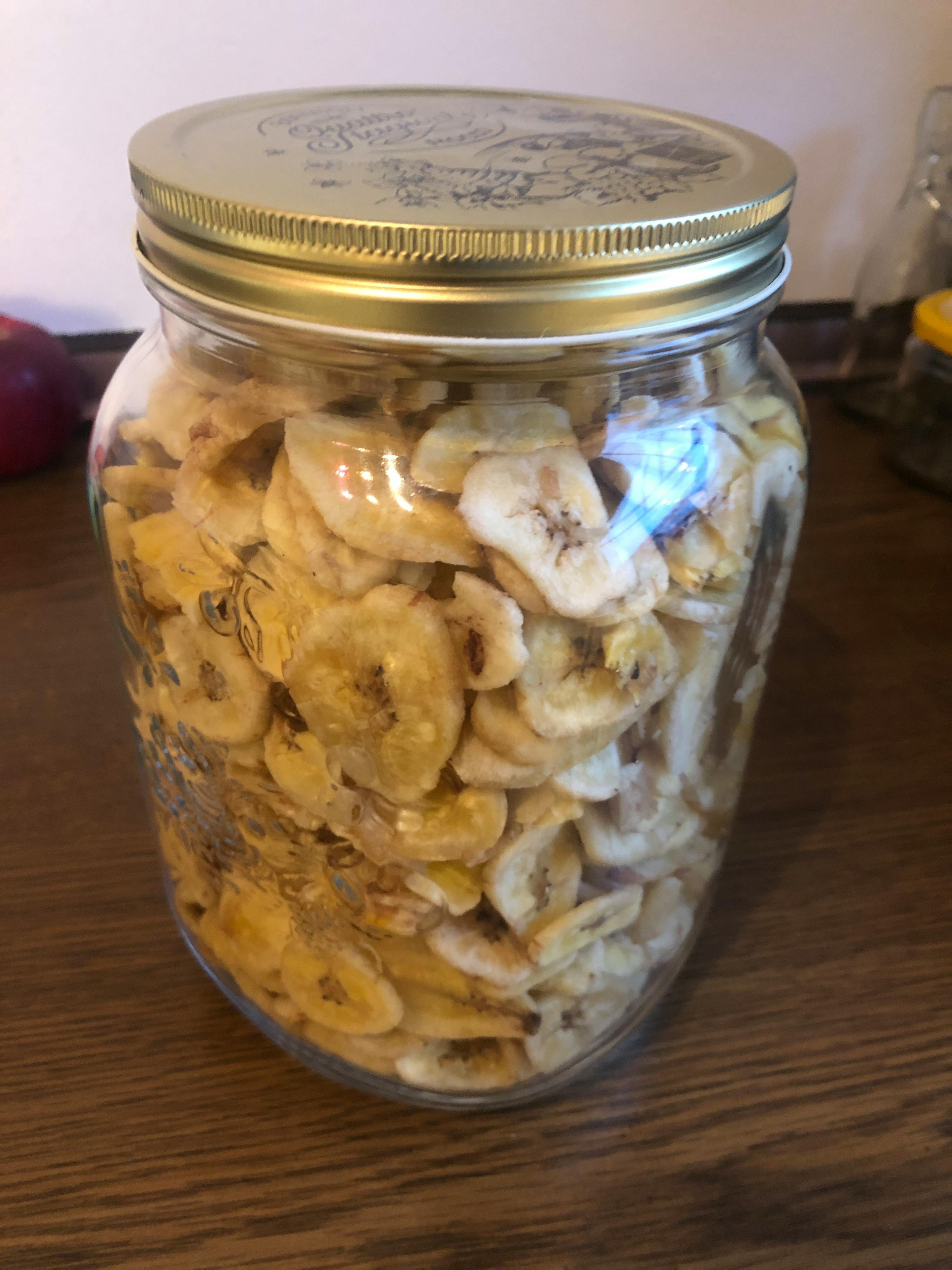 ein Glas mit Bananenchips im Deckel steht auf einem Tisch