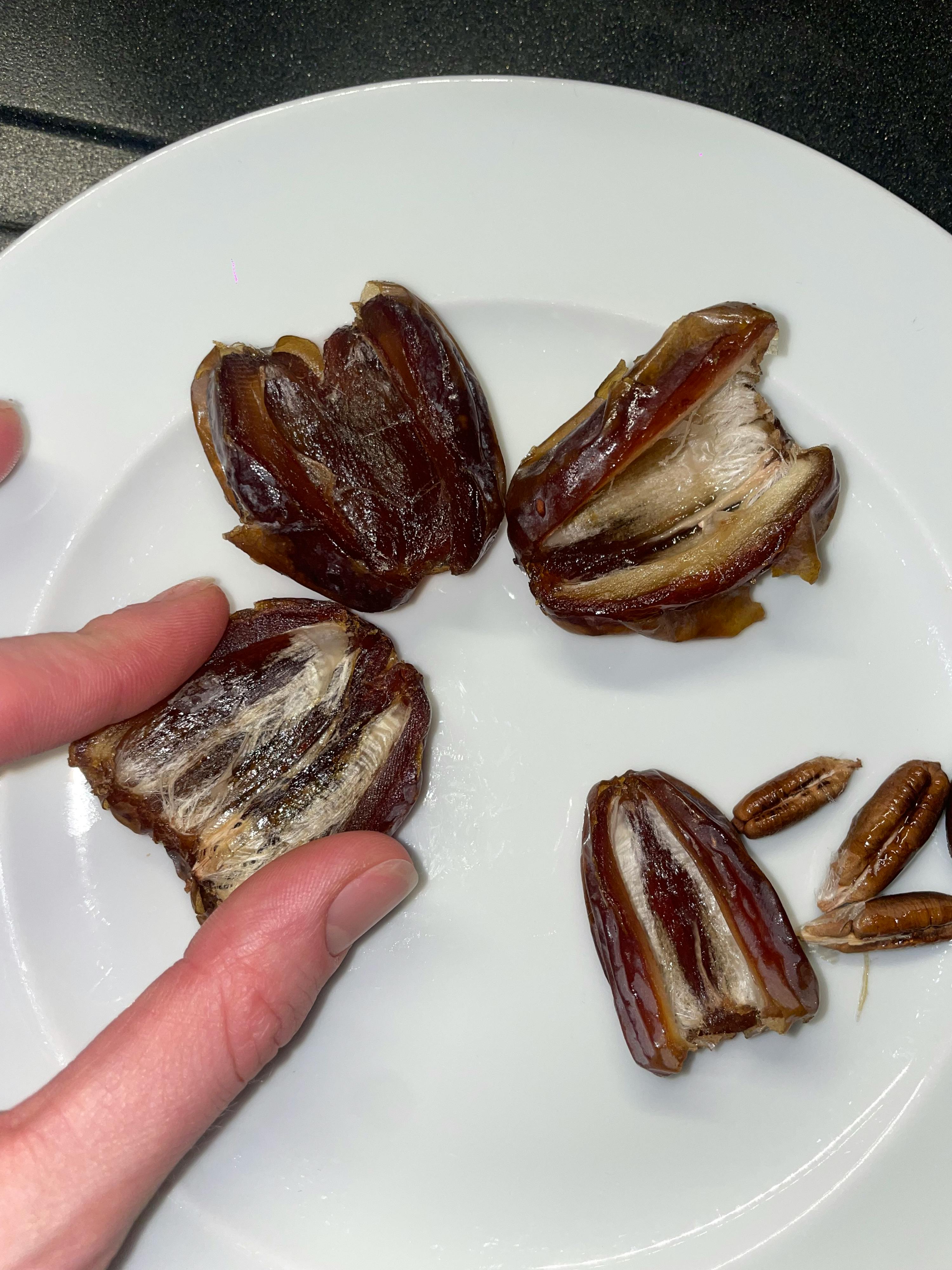 eine Person hält einen weißen Teller mit getrockneten Datteln darin