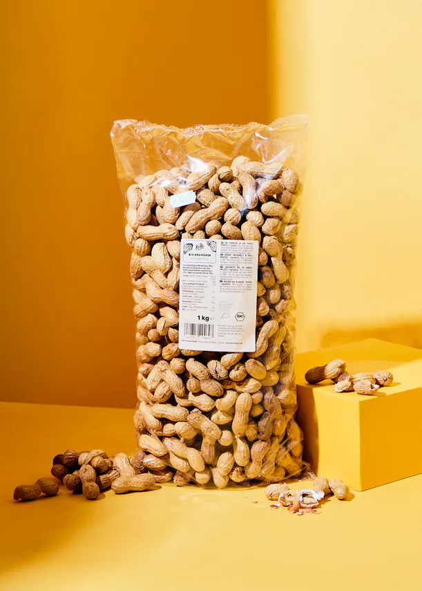 eine Tüte Erdnüsse in der Schale steht auf einer gelben Fläche