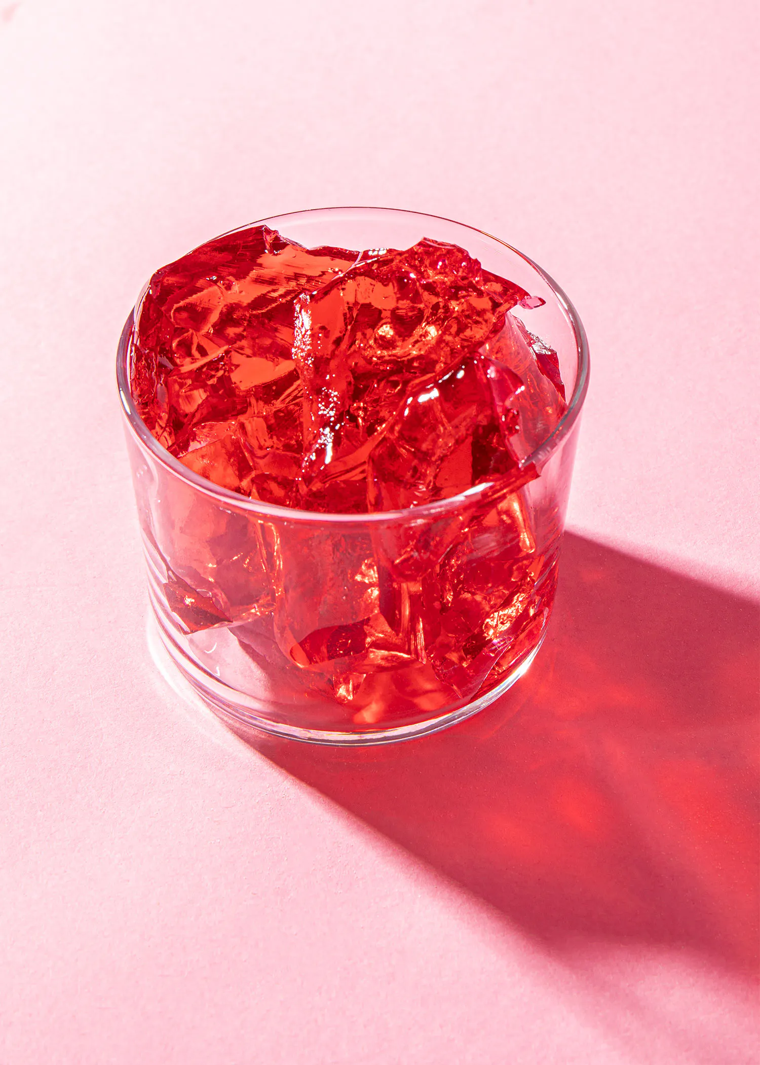 un bol en verre rempli de gelée rouge sur un fond rose
