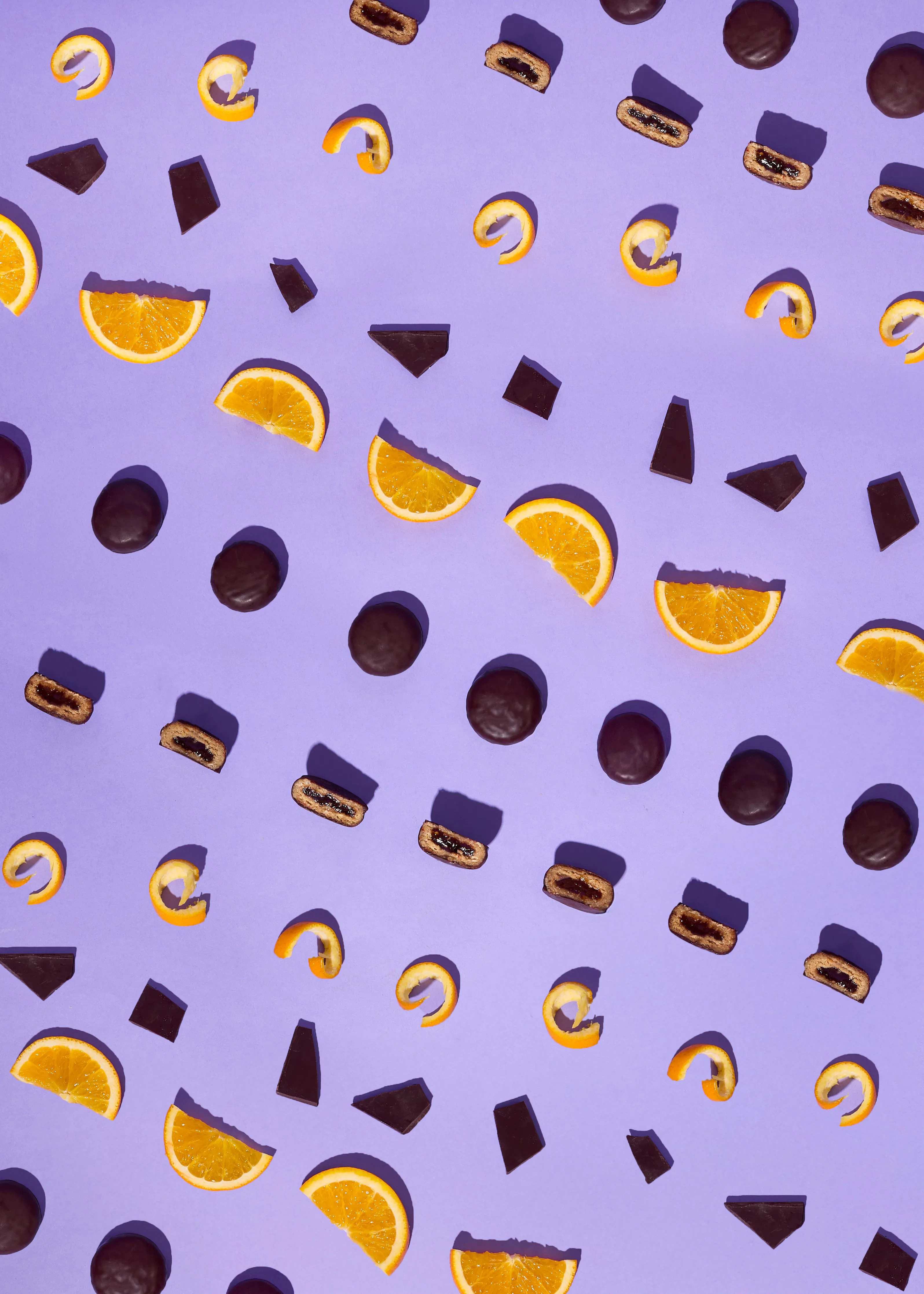 a top-down view of orange slices, orange peels, chocolate pieces, and chocolate cookies scattered across a purple background.