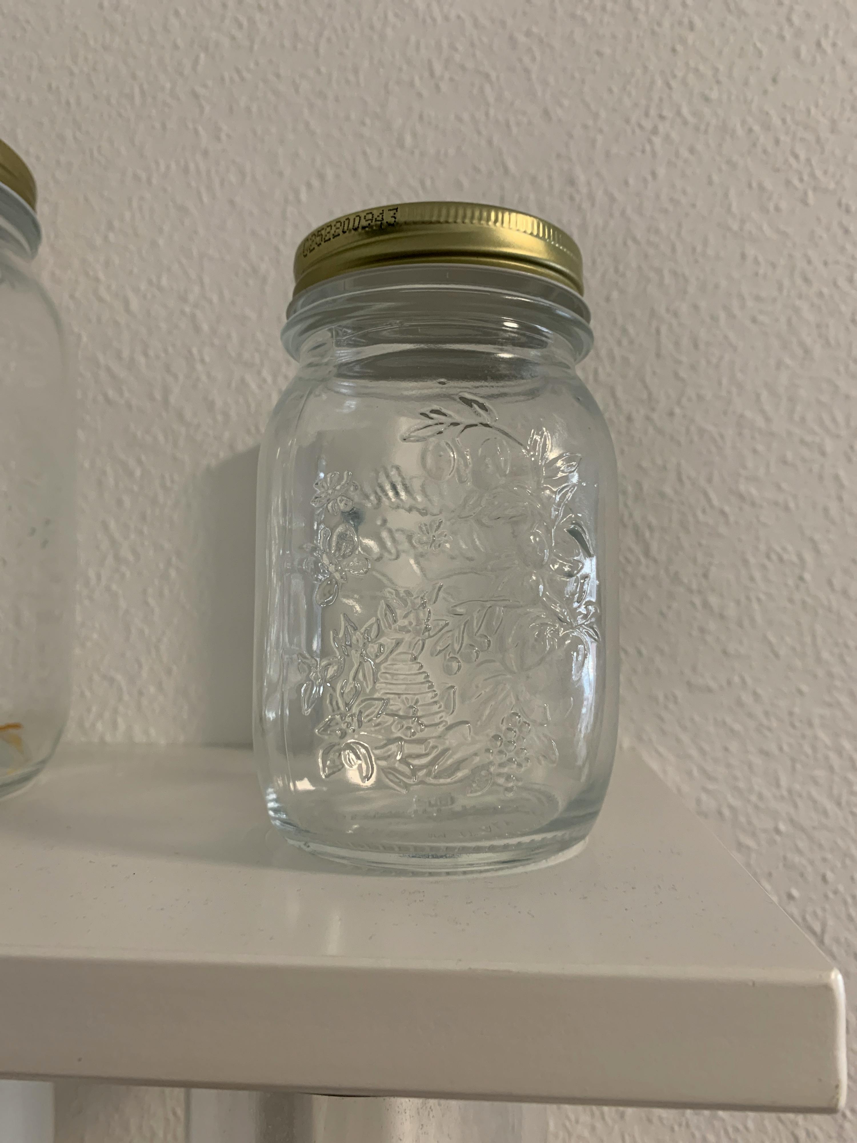 a glass jar with a gold lid sits on a white shelf