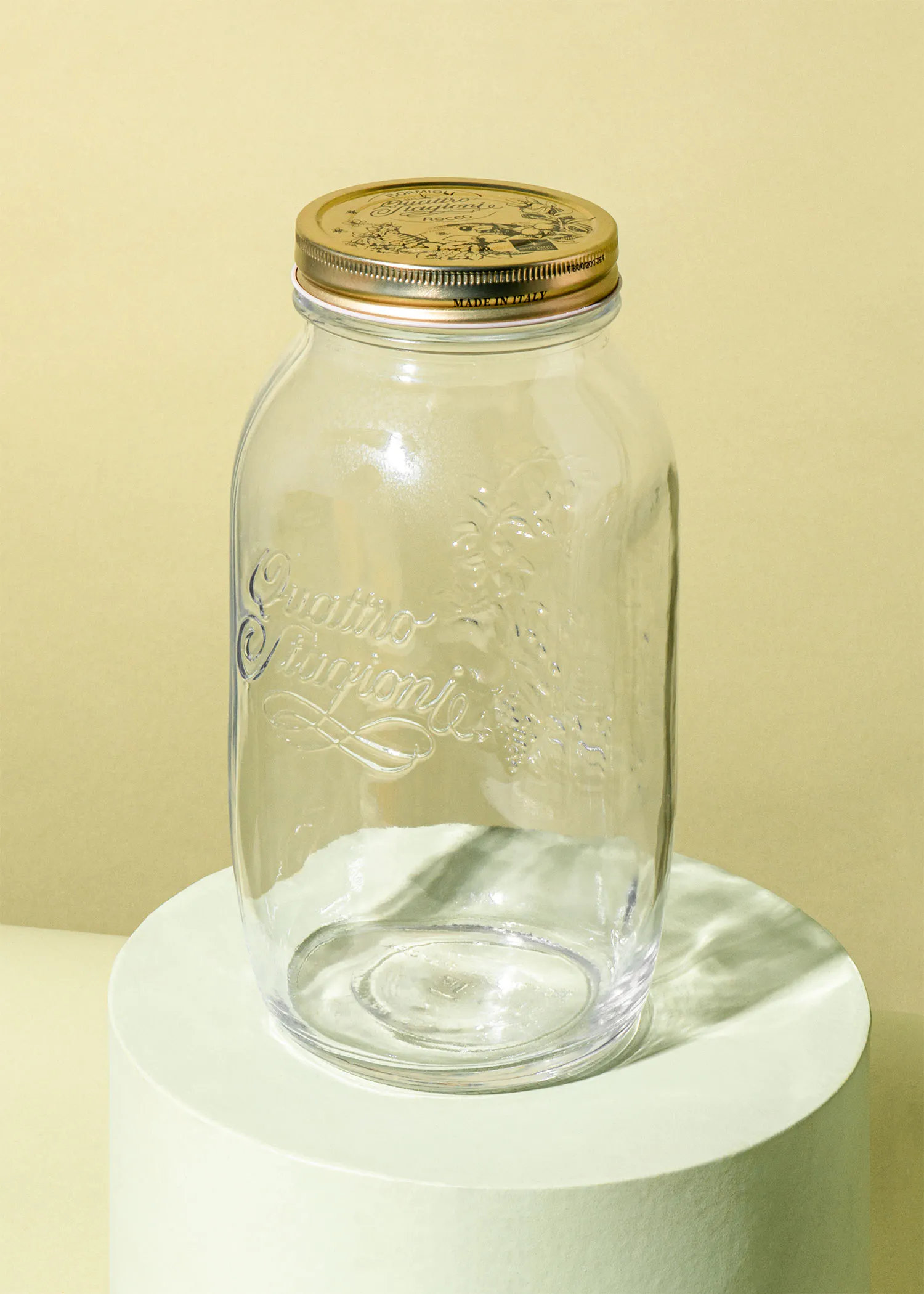 ein Glasgefäß mit einem goldenen Deckel steht auf einem weißen Sockel