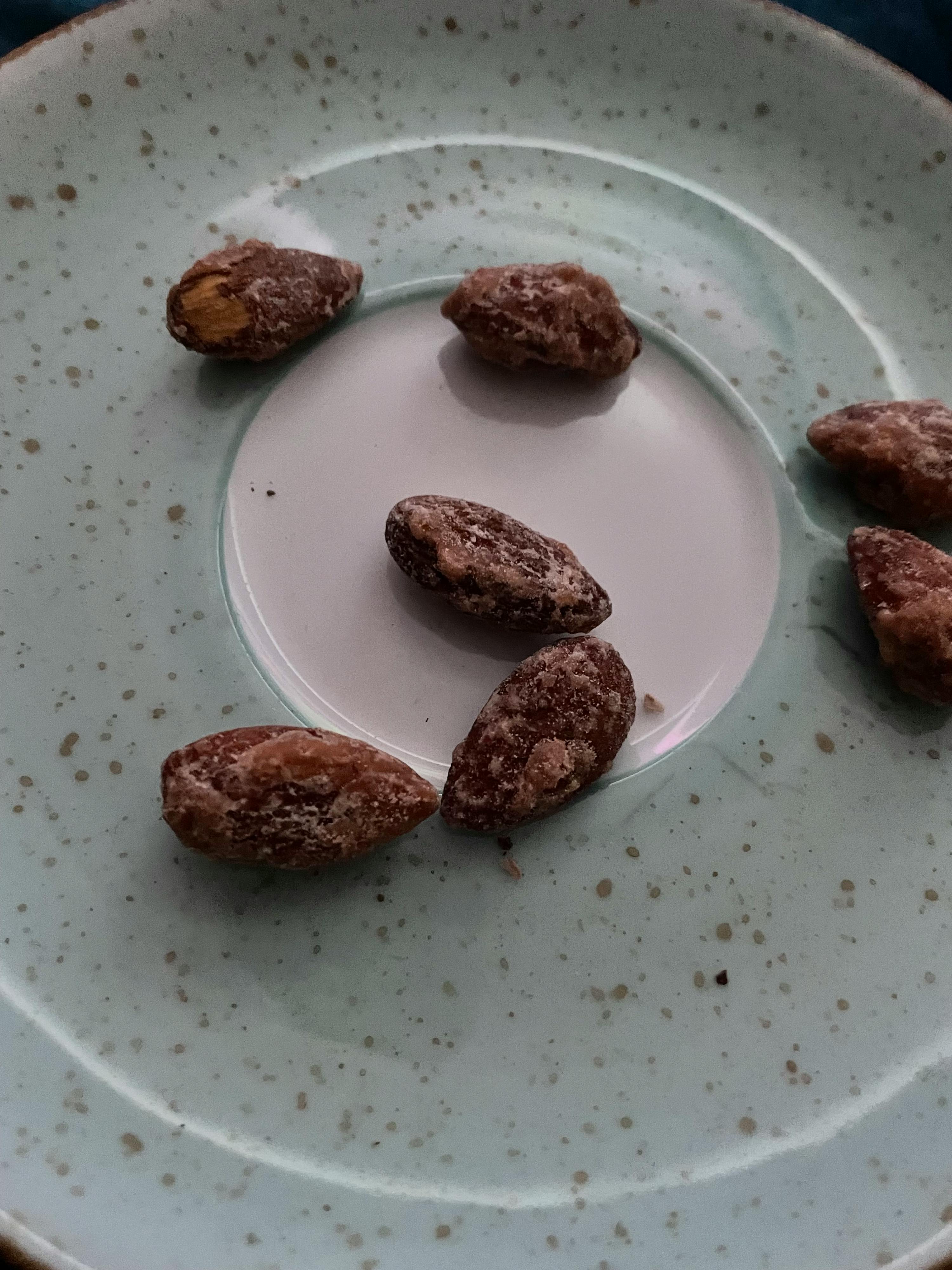 mehrere gebrannte mandeln liegen auf einem hellblauen, gesprenkelten teller.