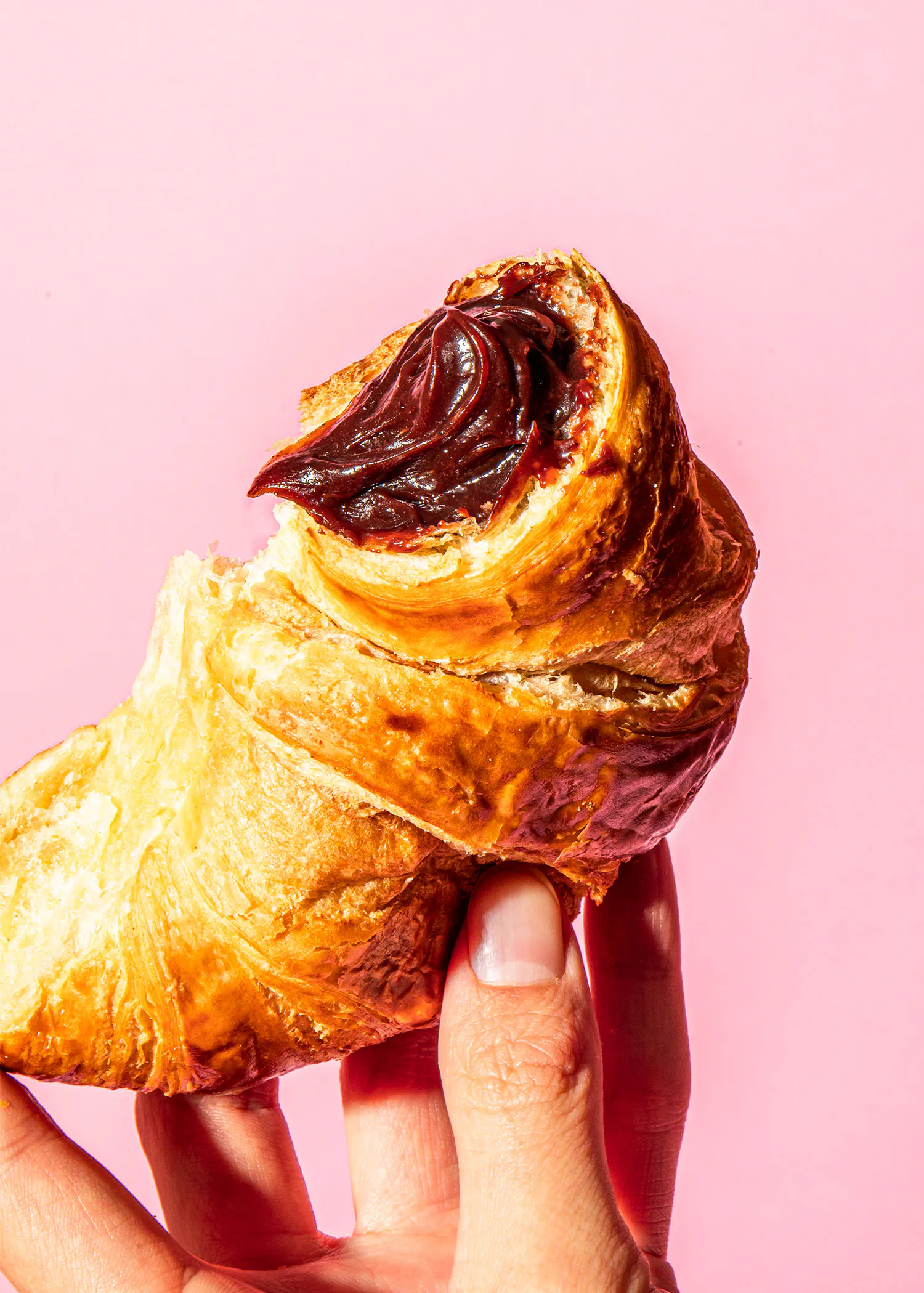 une personne tient un croissant avec de la pâte à tartiner sur un fond rose