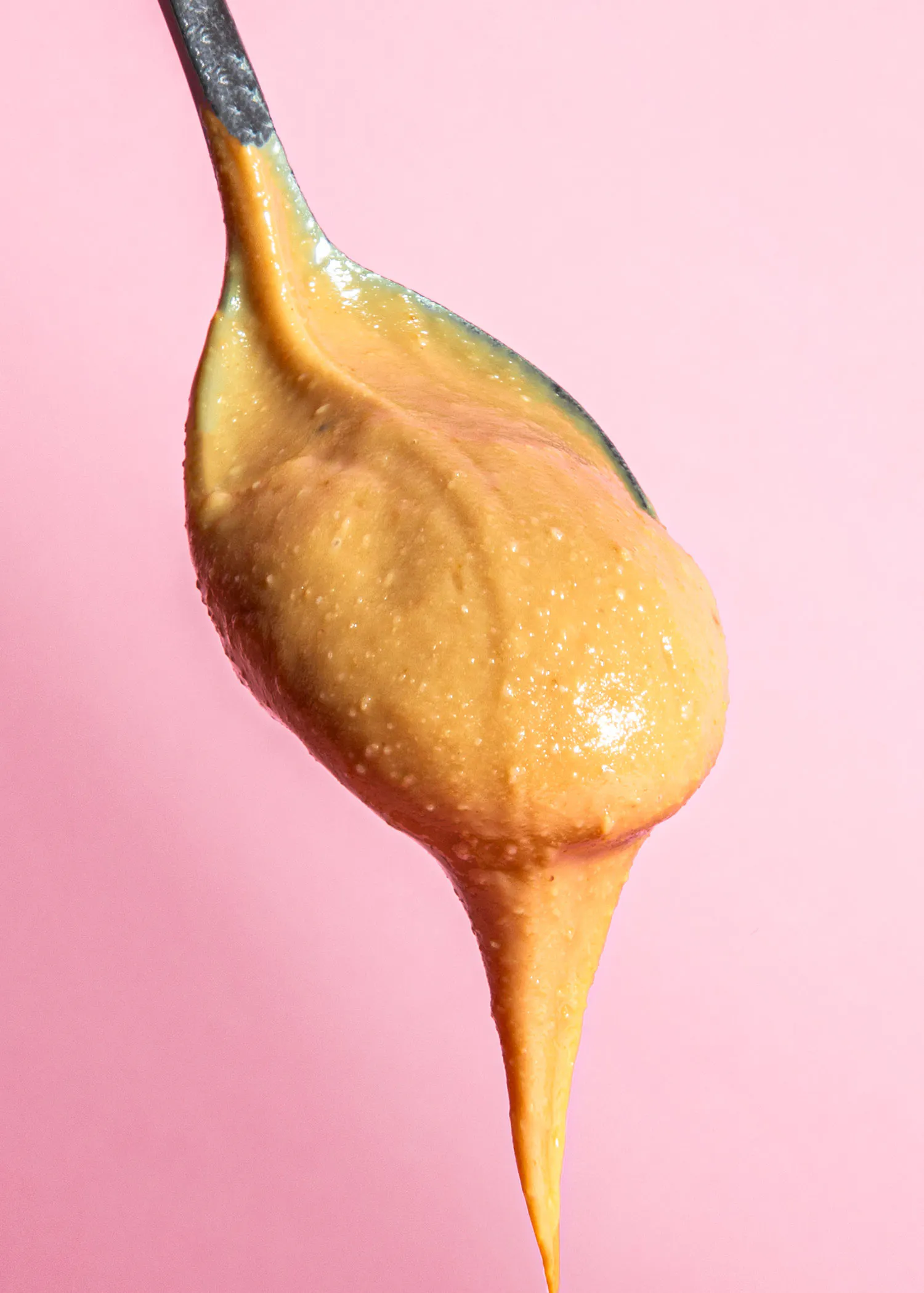 ein löffel voll erdnussbutter tropft vor einem rosa hintergrund.