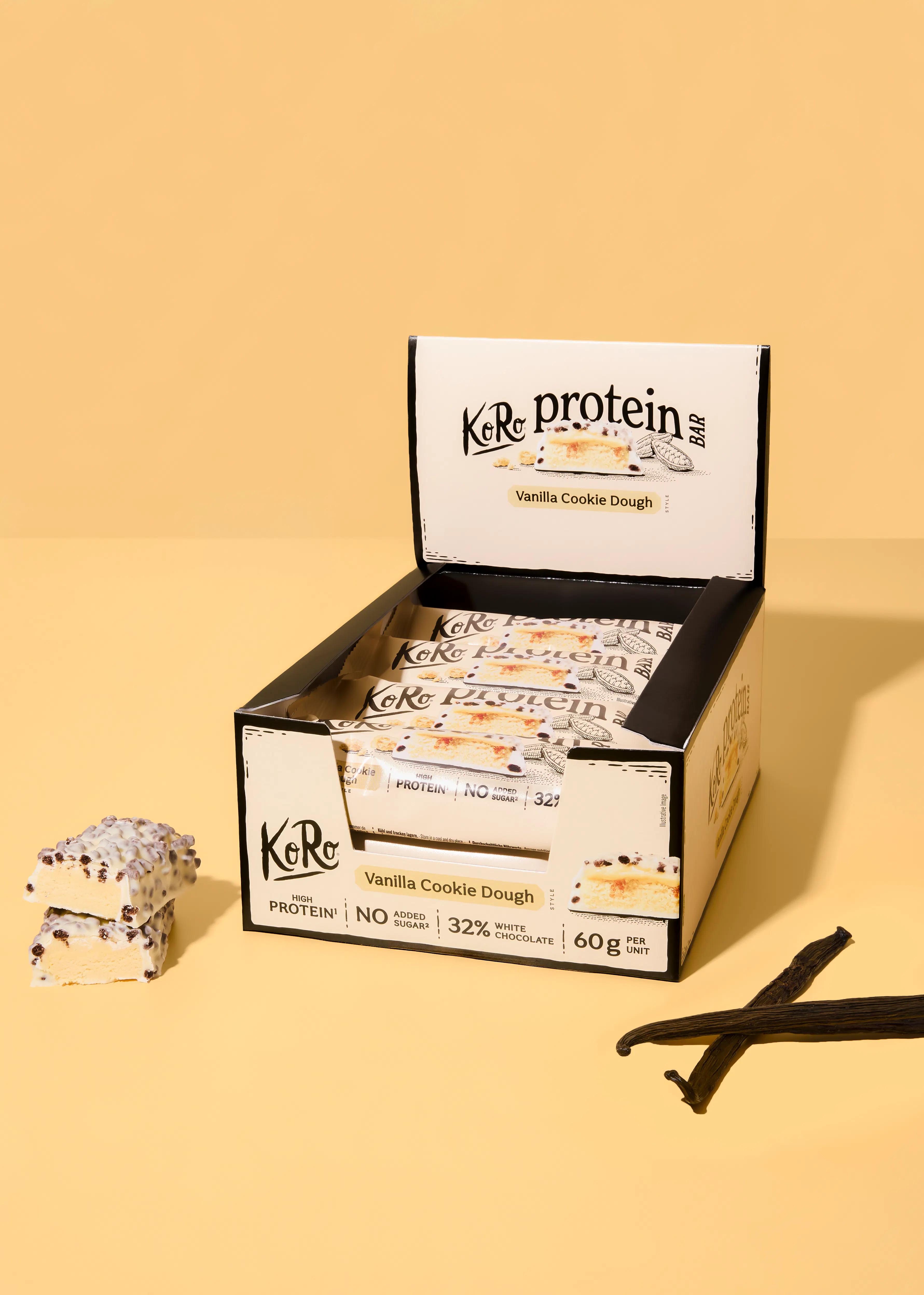 eine offene schachtel mit koro protein vanille-cookie-dough-riegeln, zwei riegel daneben und vanilleschoten auf einem gelben hintergrund.