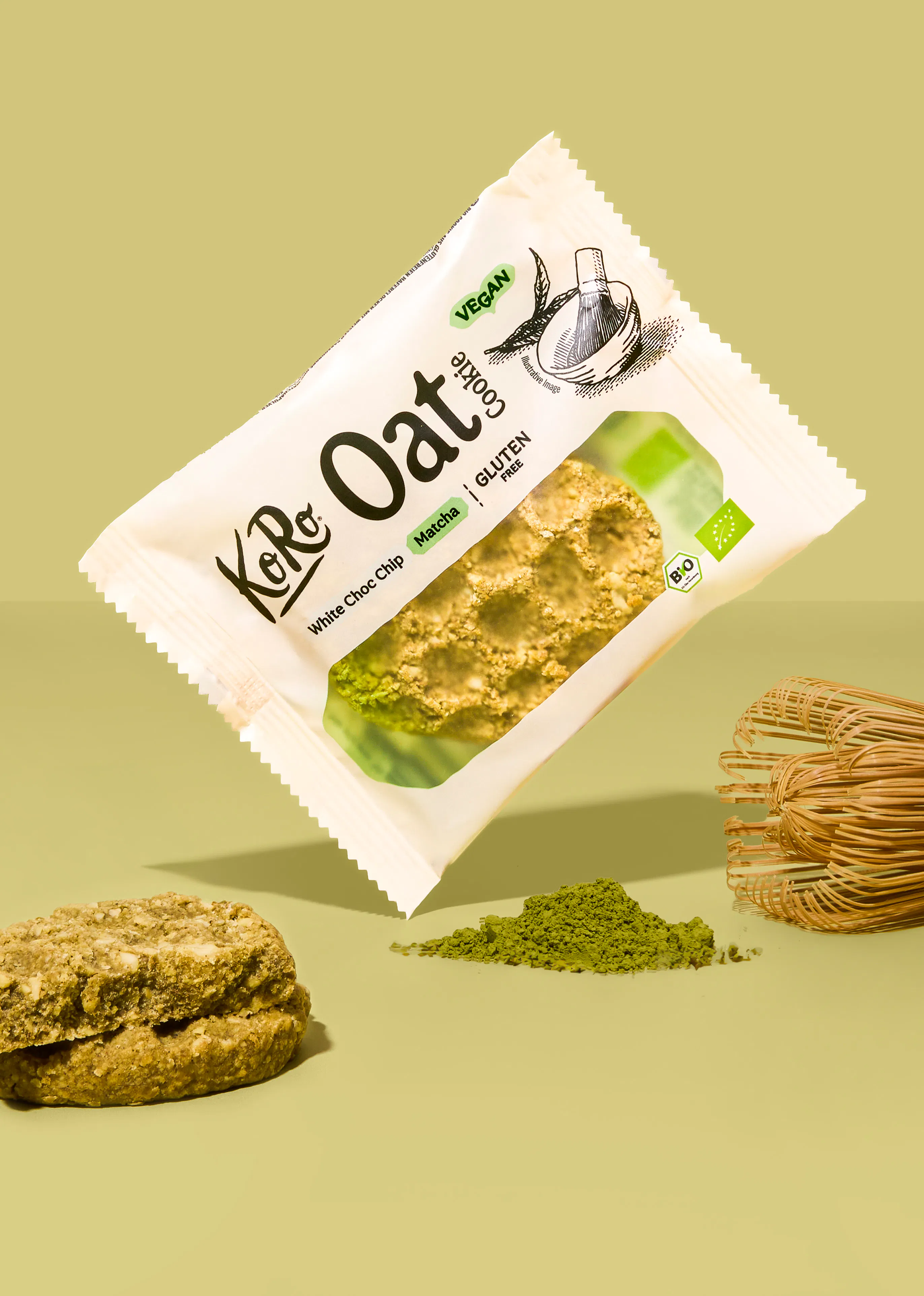 un paquet de cookie à l'avoine koro au matcha et pépites de chocolat blanc flottant au-dessus d'un cookie, d'un tas de poudre de matcha et d'un fouet en bambou sur un fond vert.