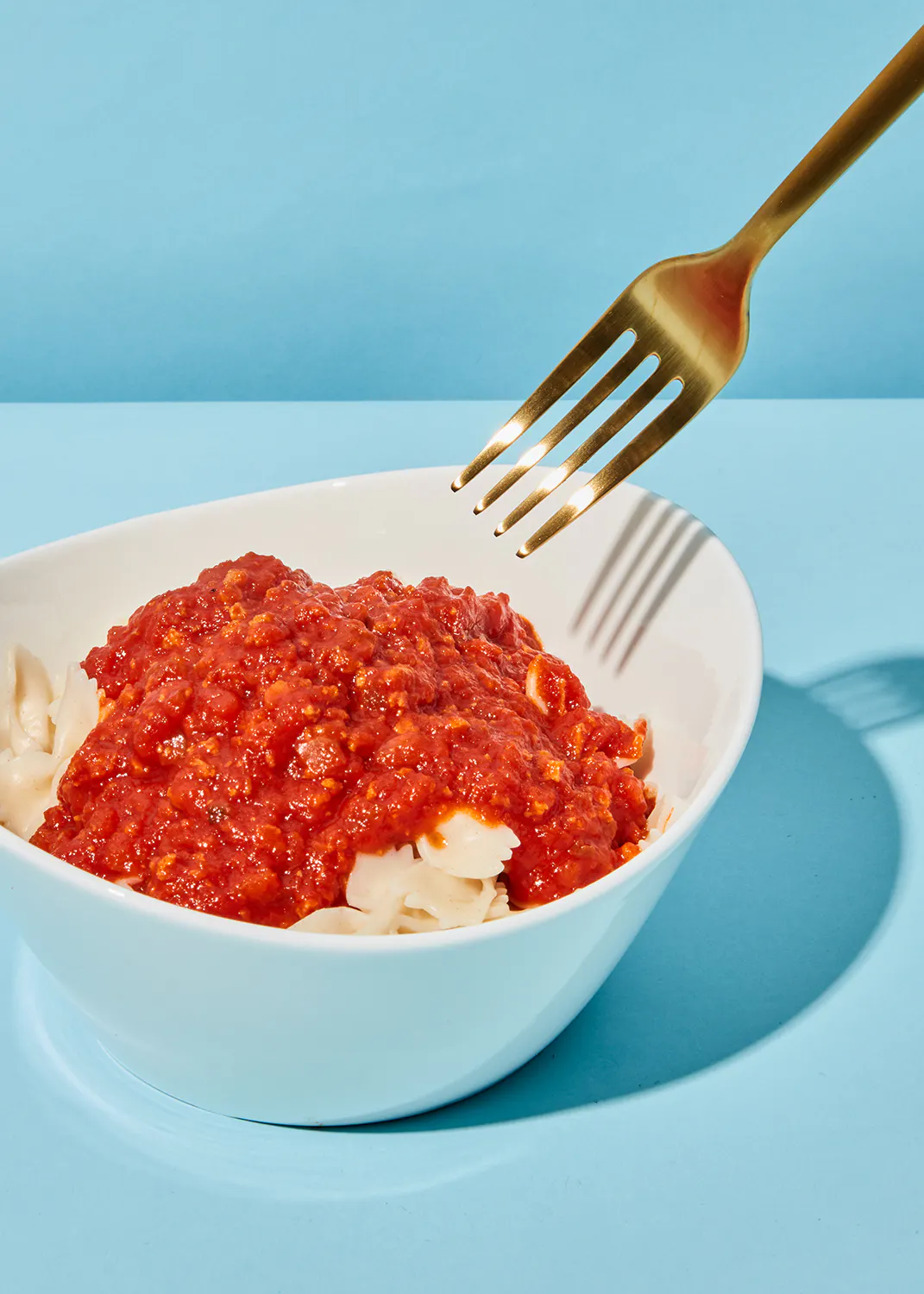 eine weiße Schüssel mit Nudeln und Tomatensoße mit einer goldenen Gabel darin