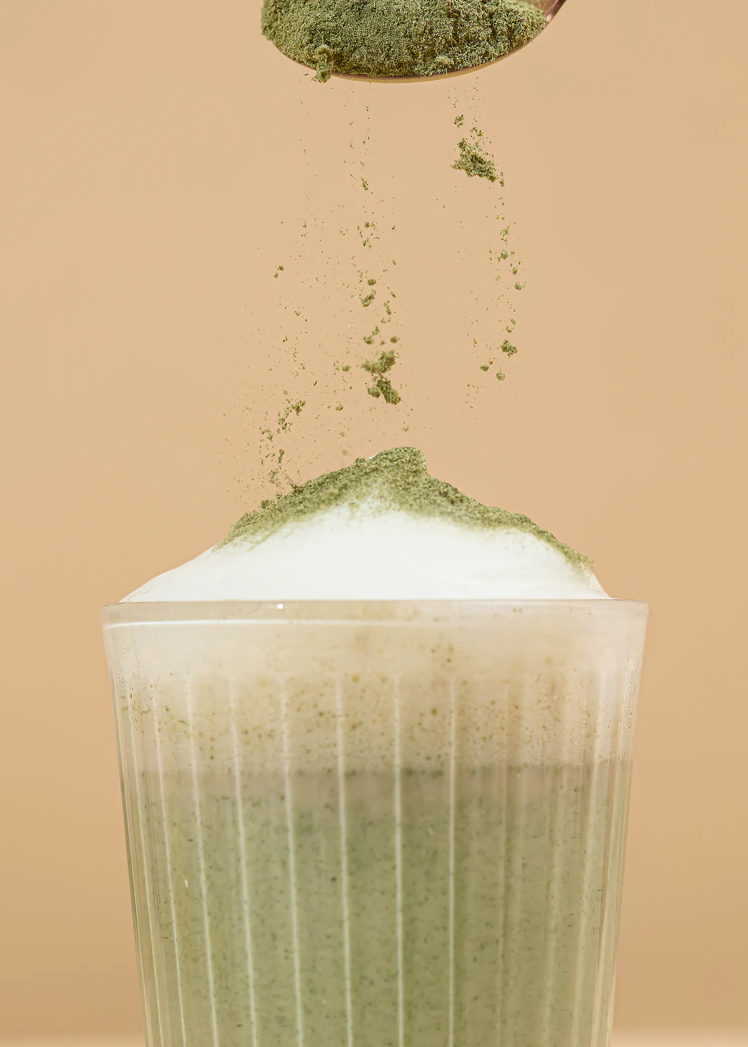 une cuillère remplie de poudre verte est versée dans un verre de boisson