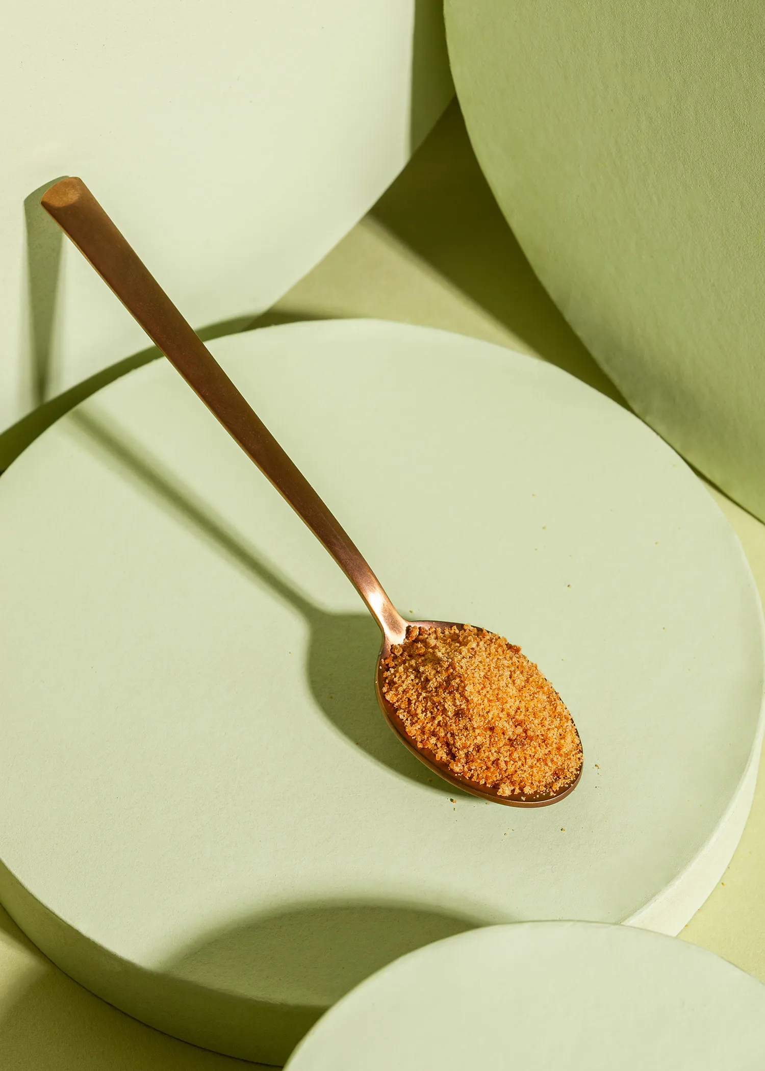 a copper spoon filled with brown powder on a green surface