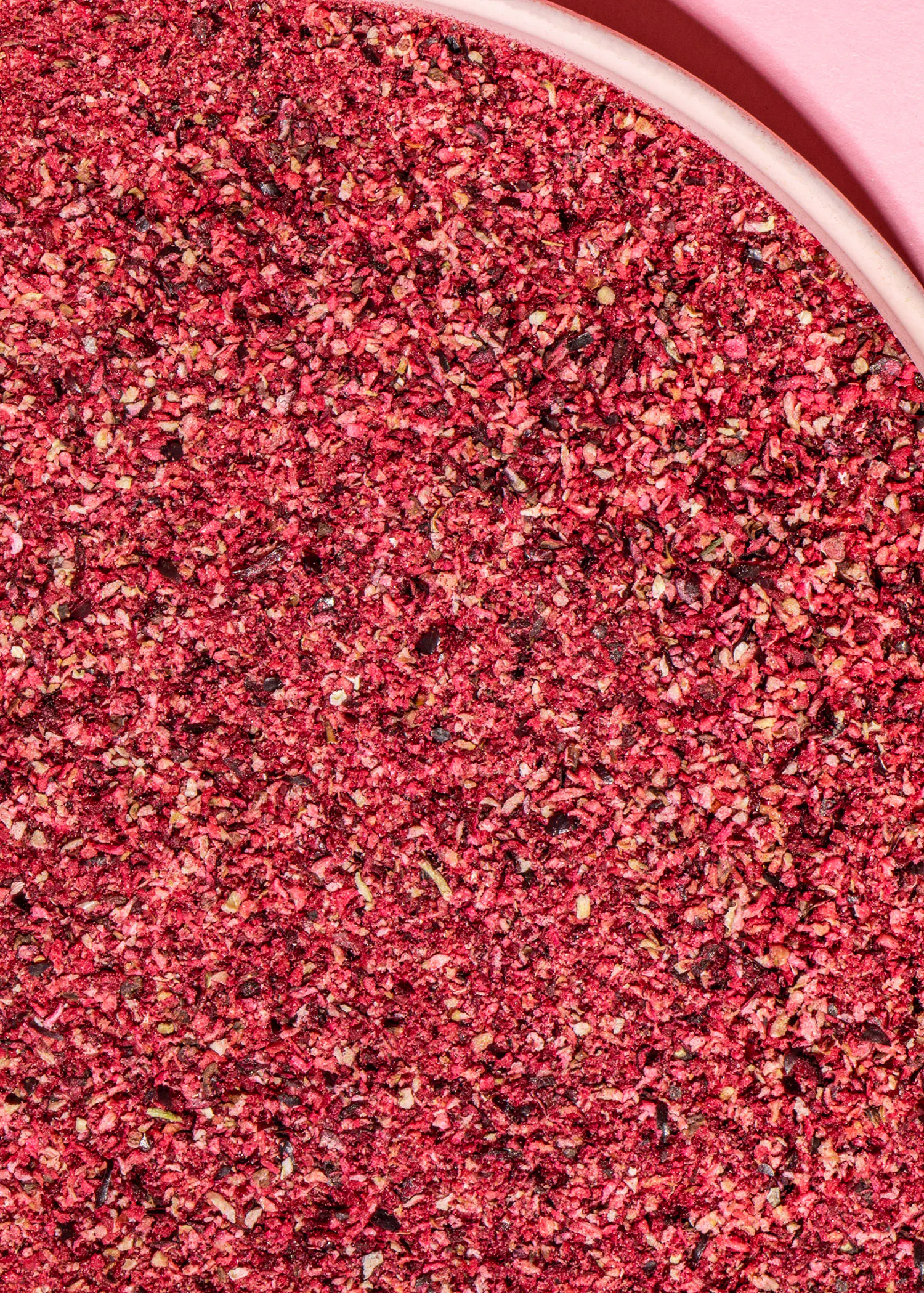 un gros plan d' un bol rempli de graines rouges sur fond rose