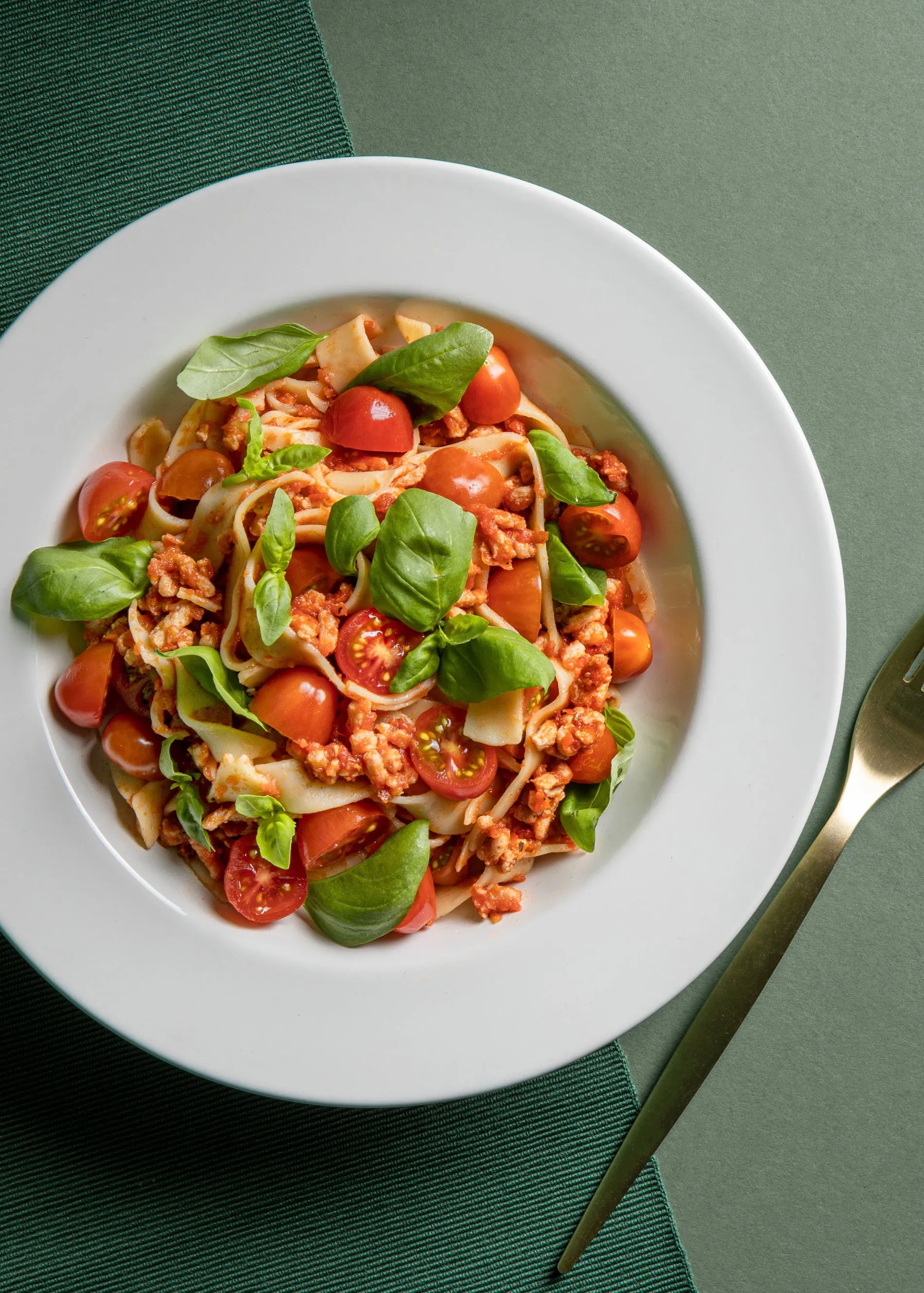 a plate of pasta with tomatoes and basil next to a fork