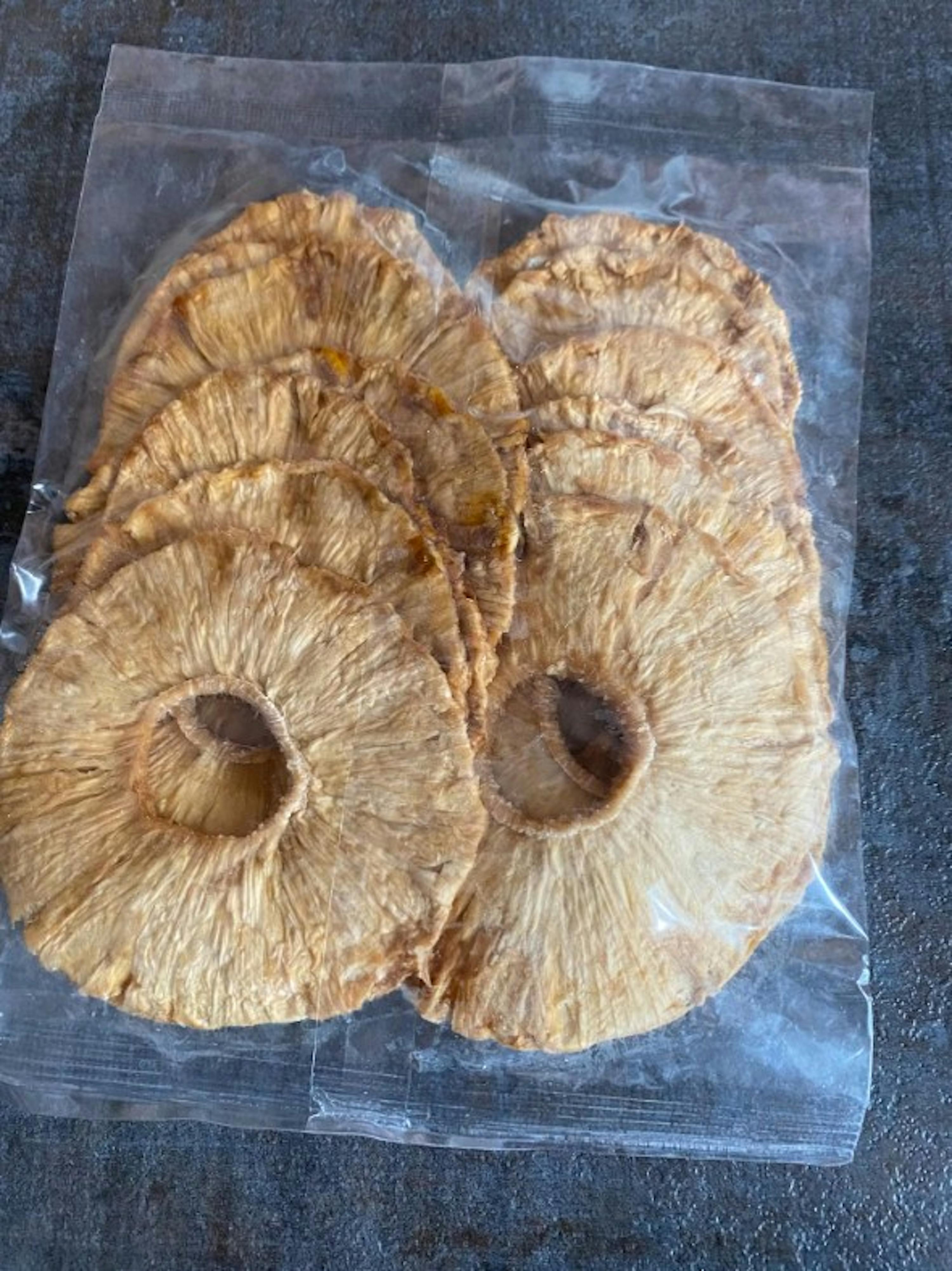 fette di ananas essiccato di colore dorato, confezionate in un sacchetto di plastica trasparente.