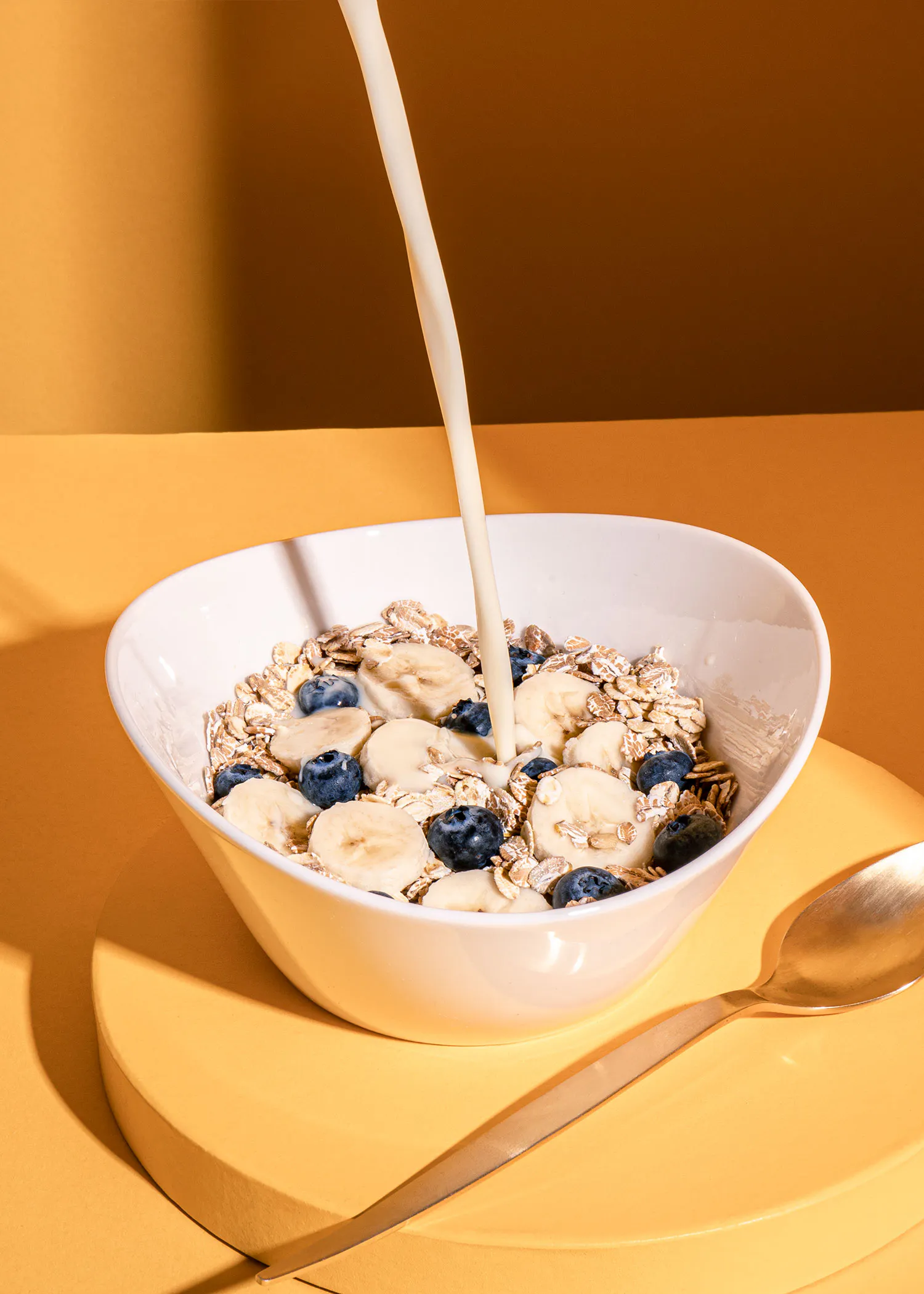 un bol de céréales avec des bananes et des myrtilles est versé avec une cuillère