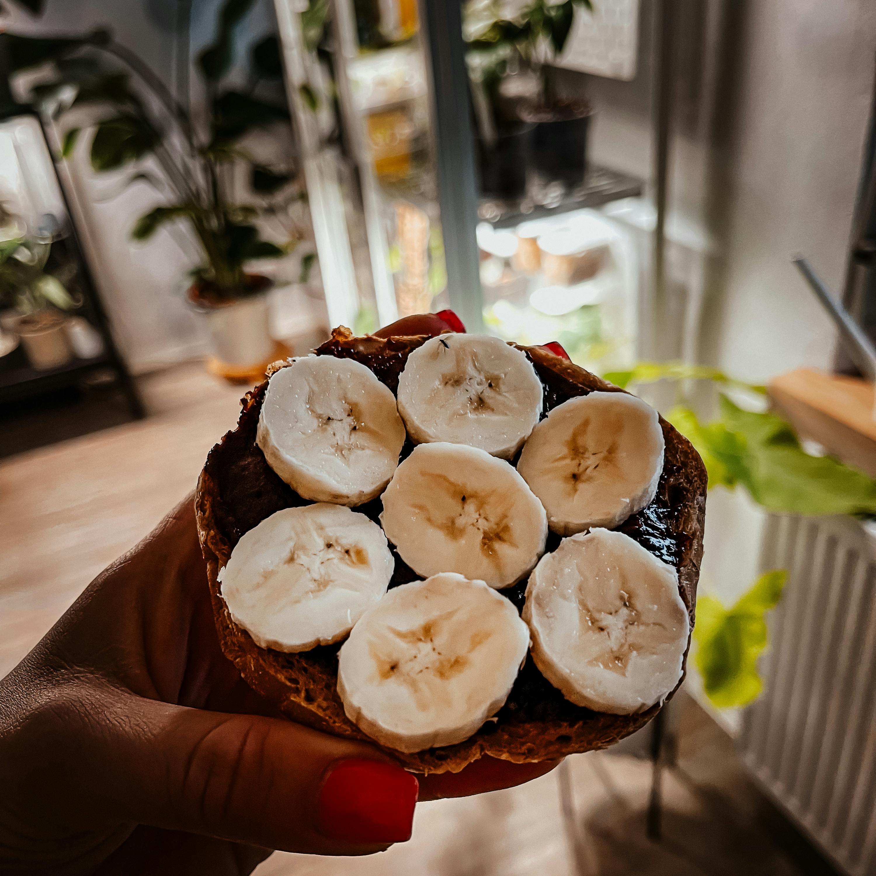 a person holding a sandwich with sliced bananas on top