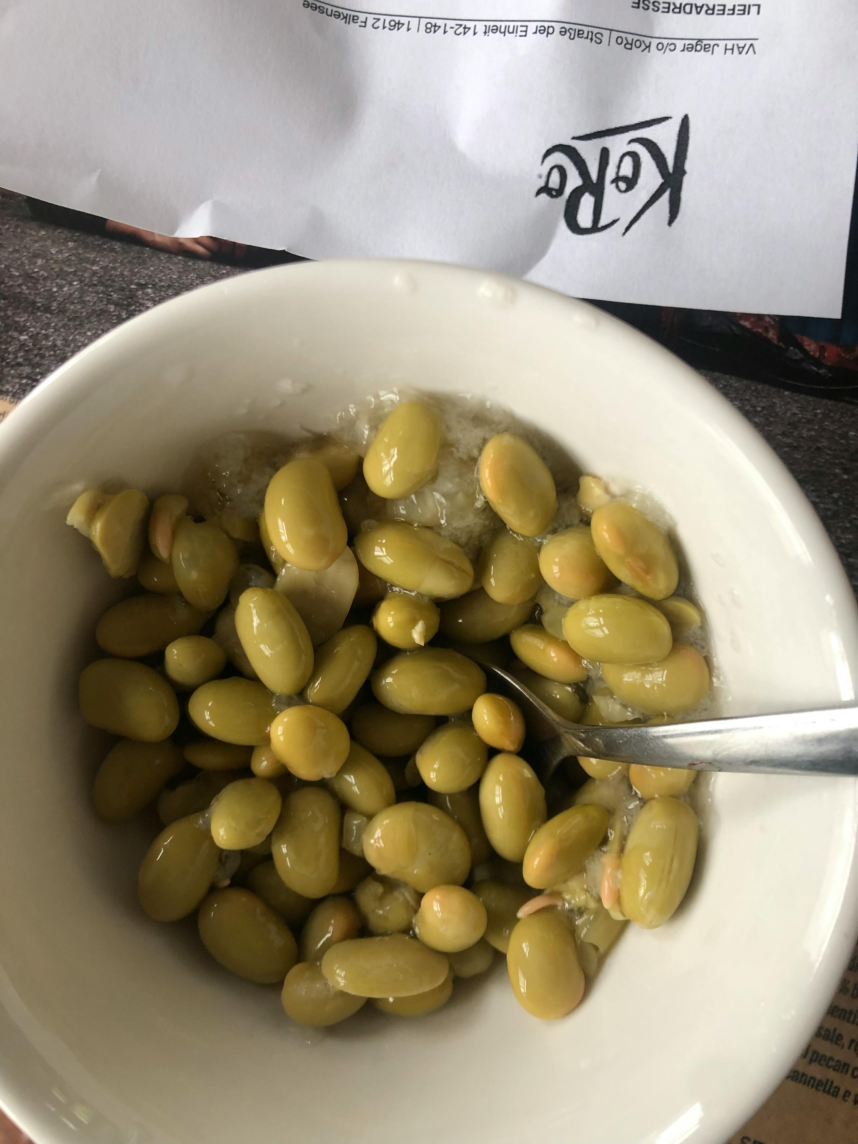 eine weiße Schüssel mit grünen Bohnen und einem Löffel darauf