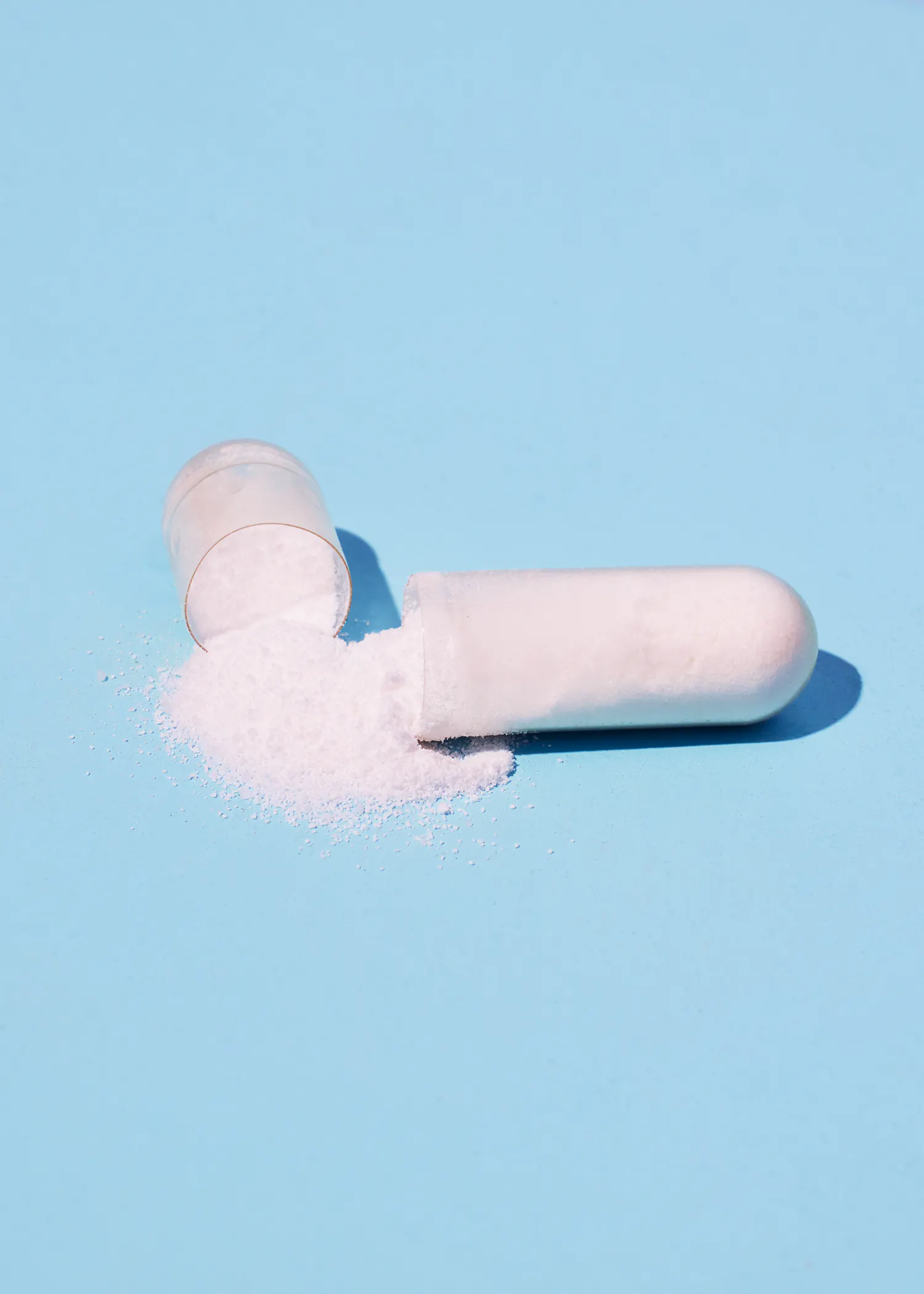 a white capsule with powder pouring out of it on a blue surface