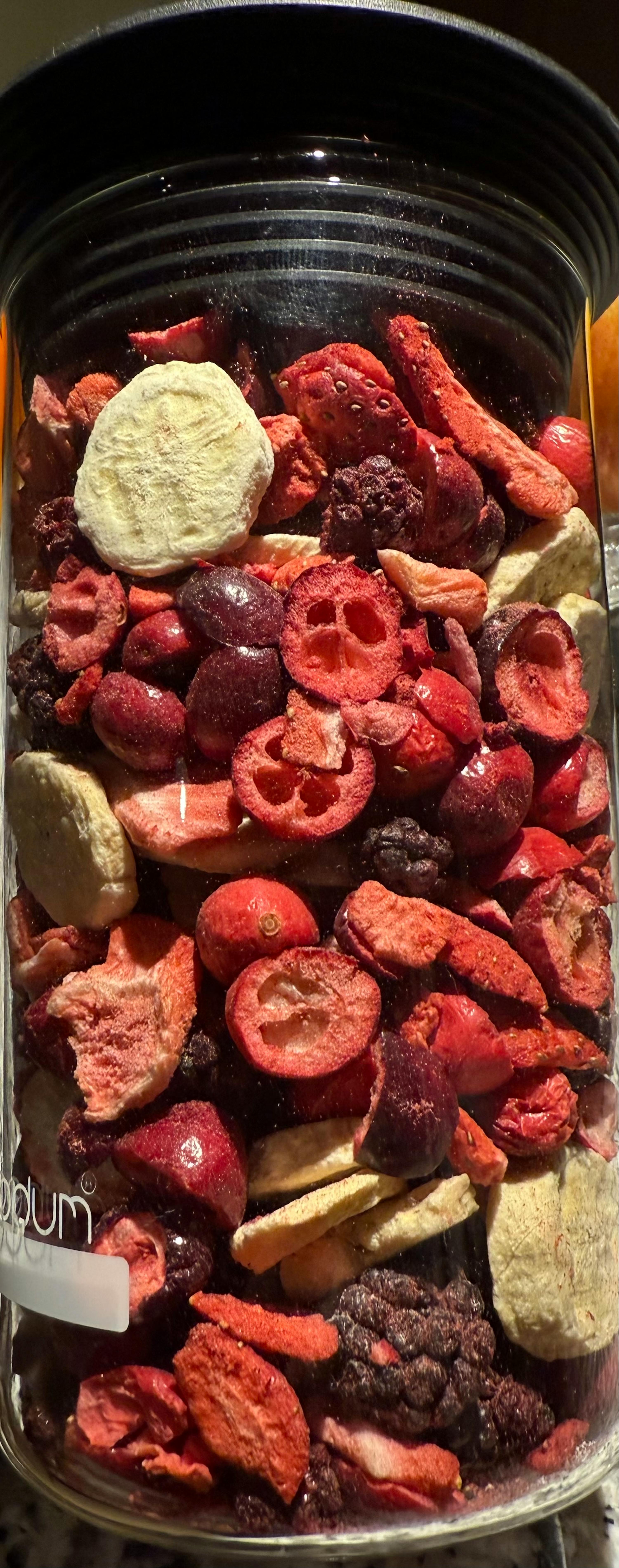 un barattolo trasparente pieno di frutta secca mista, con bacche rosse, fragole essiccate e fette di banana.