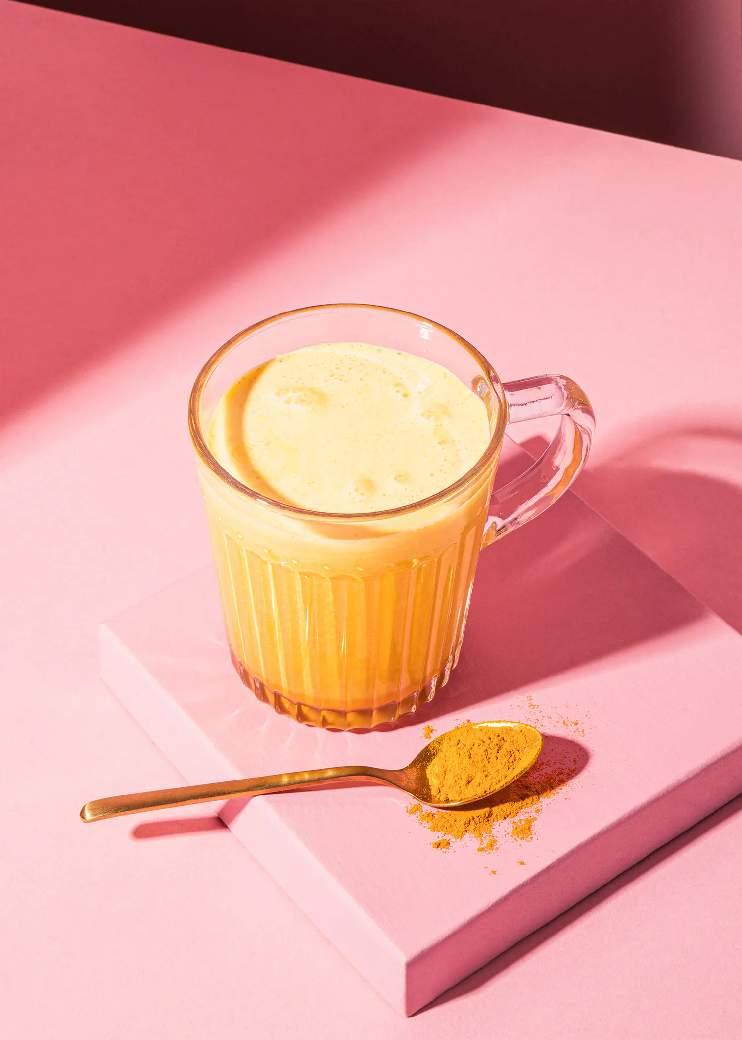 a cup of yellow liquid next to a spoon of turmeric