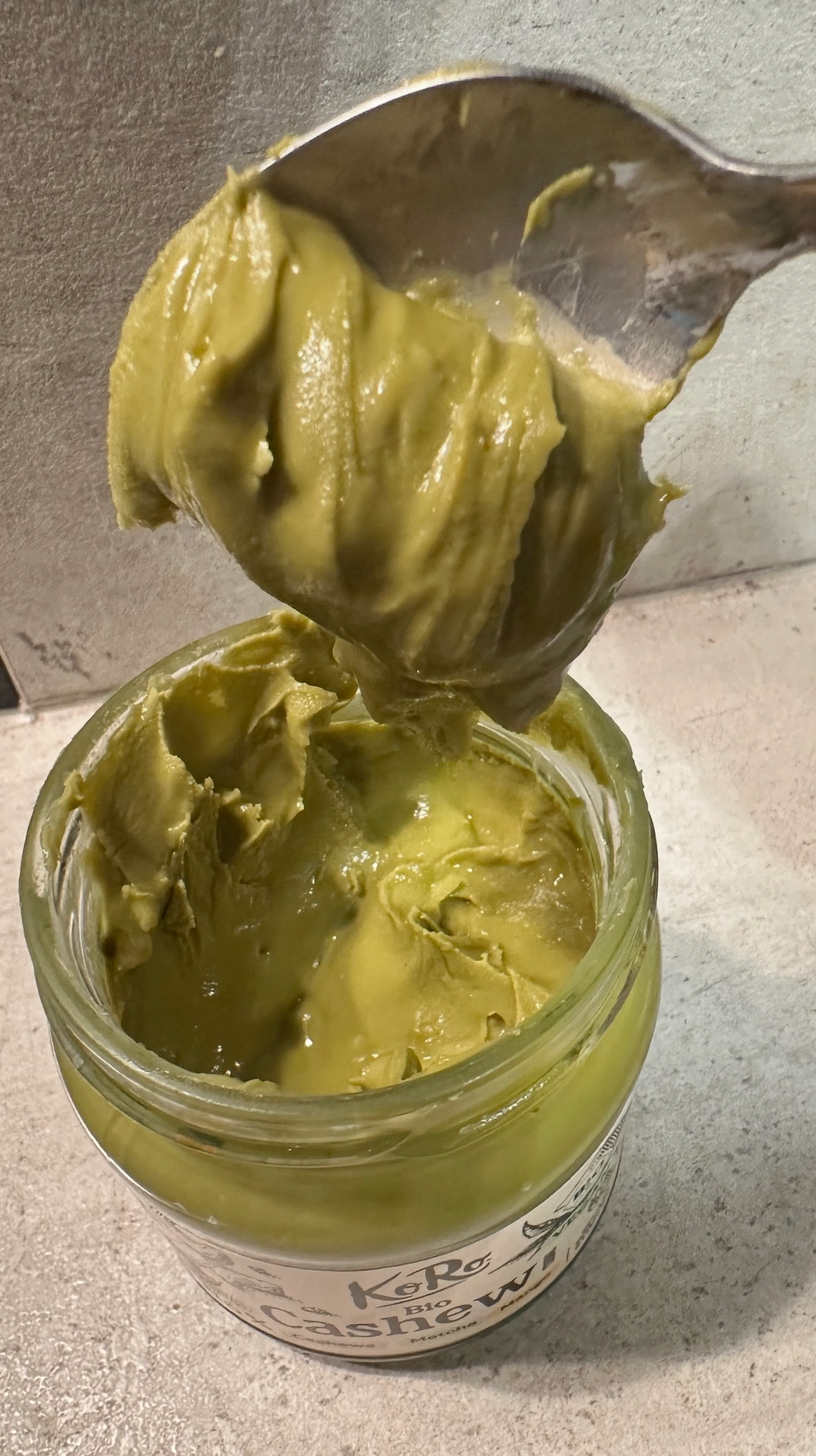 ein löffel schöpft grüne cashew-matcha-creme aus einem glas.