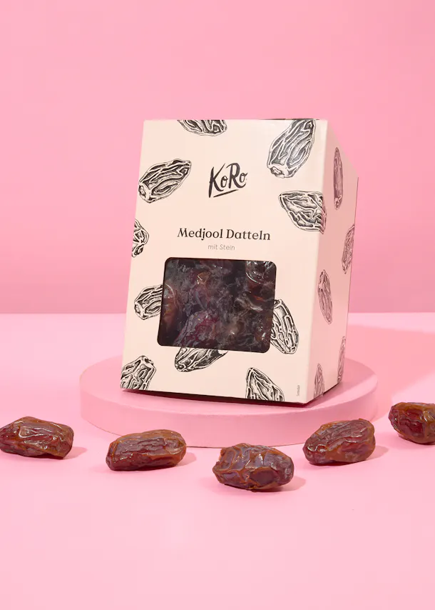 eine Schachtel mit medjool datteln steht auf einem rosa Tisch