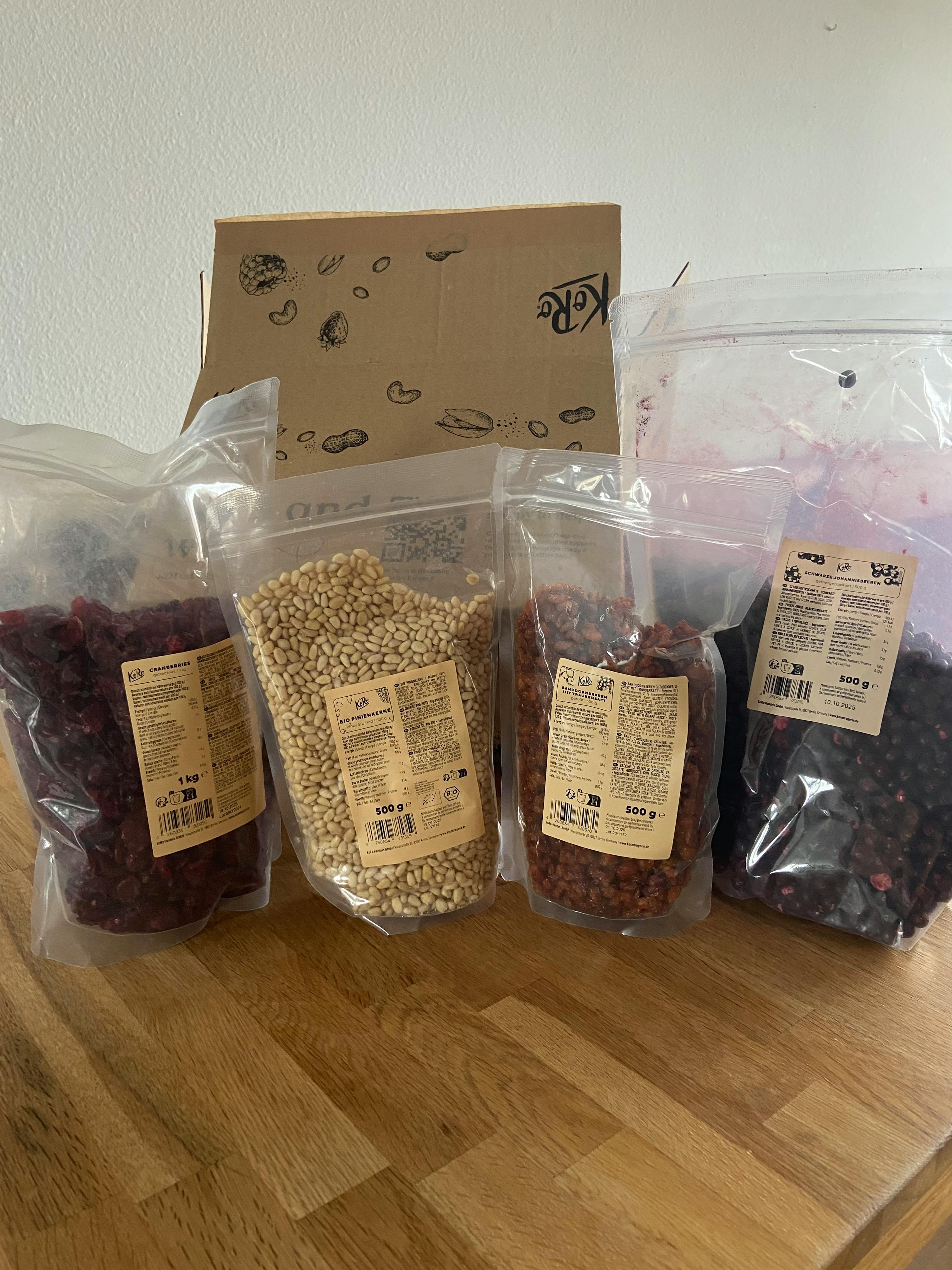 several bags of food including pine nuts and cranberries are on a wooden table