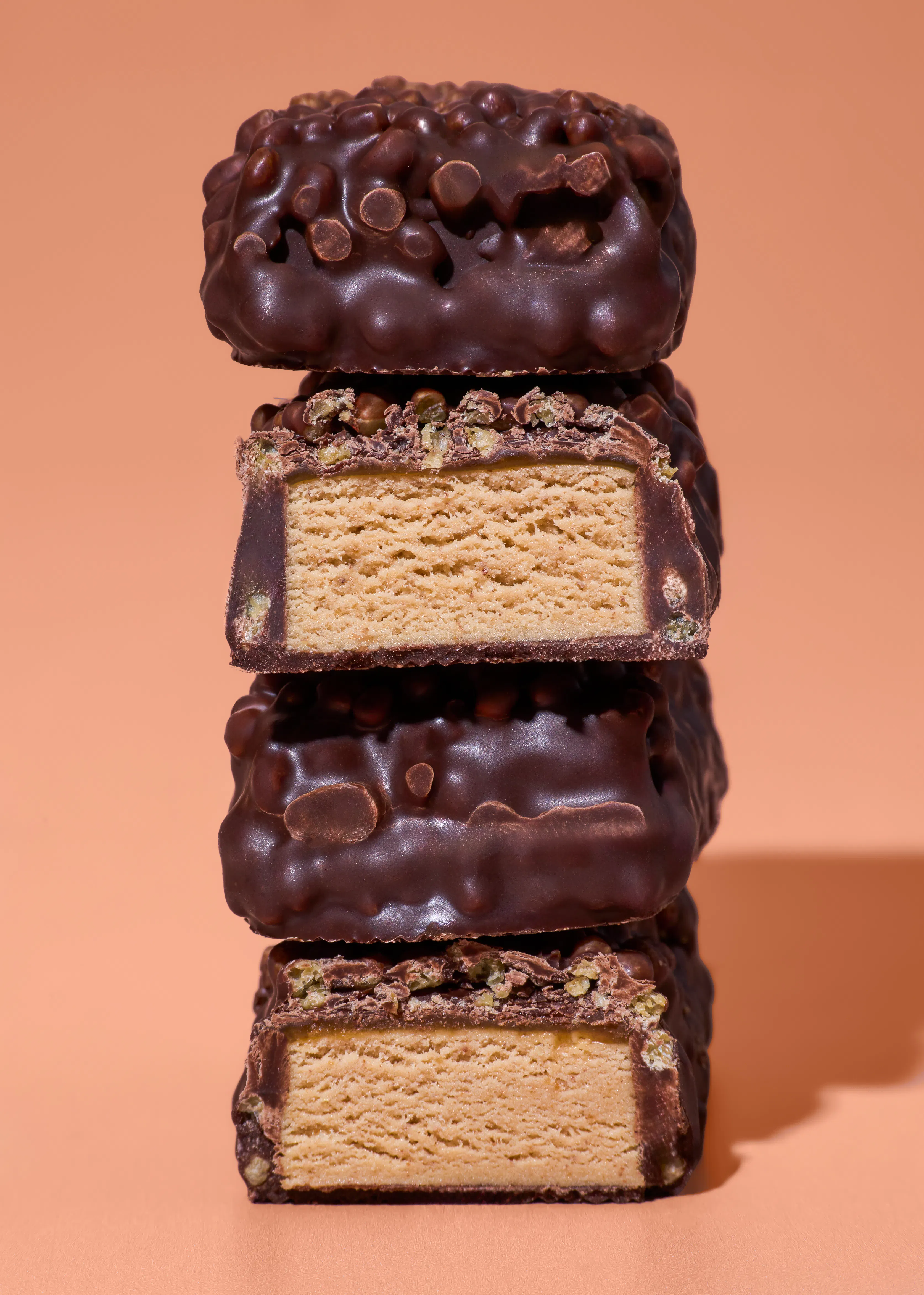 a stack of four chocolate-covered bars, two of which are cut in half to reveal a light-colored, dense filling, against a light brown background.