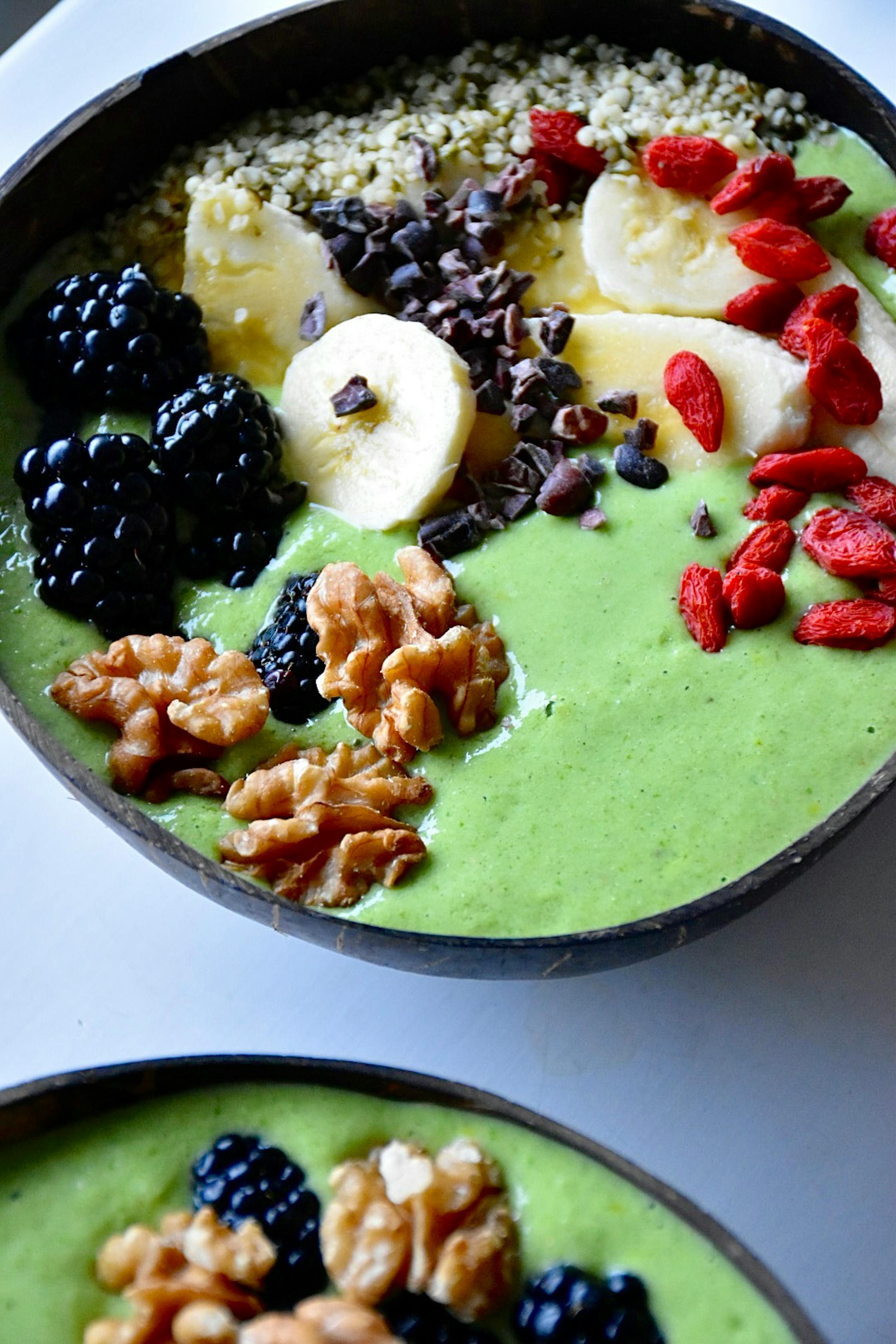 a bowl of green smoothie with bananas blackberries walnuts and goji berries on top