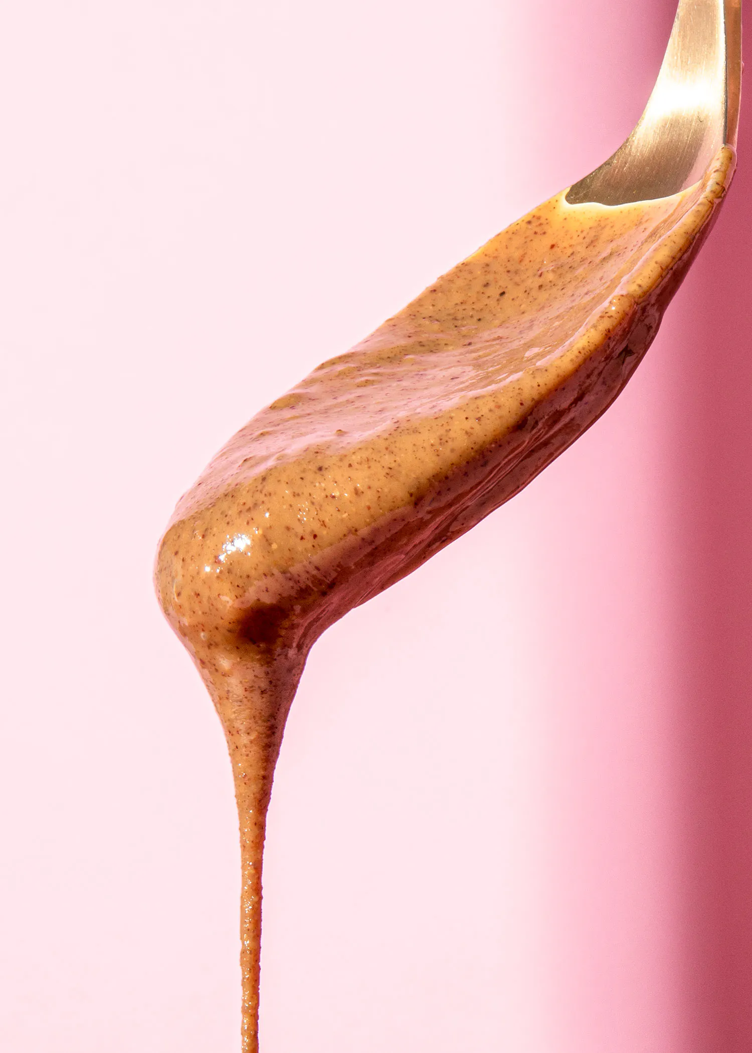 une cuillère remplie de sauce brune sur fond rose