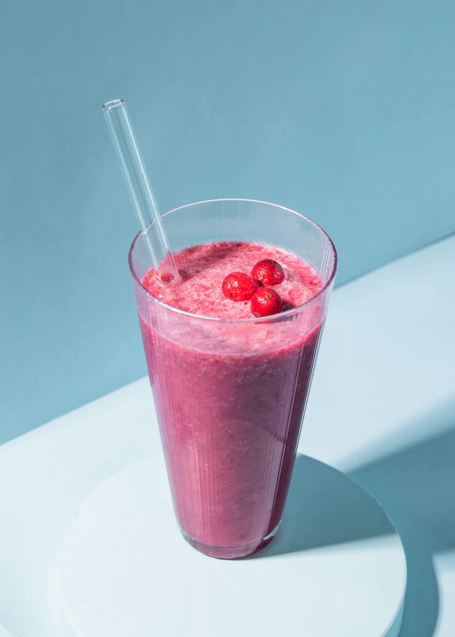 a smoothie in a glass with a clear straw and berries on top