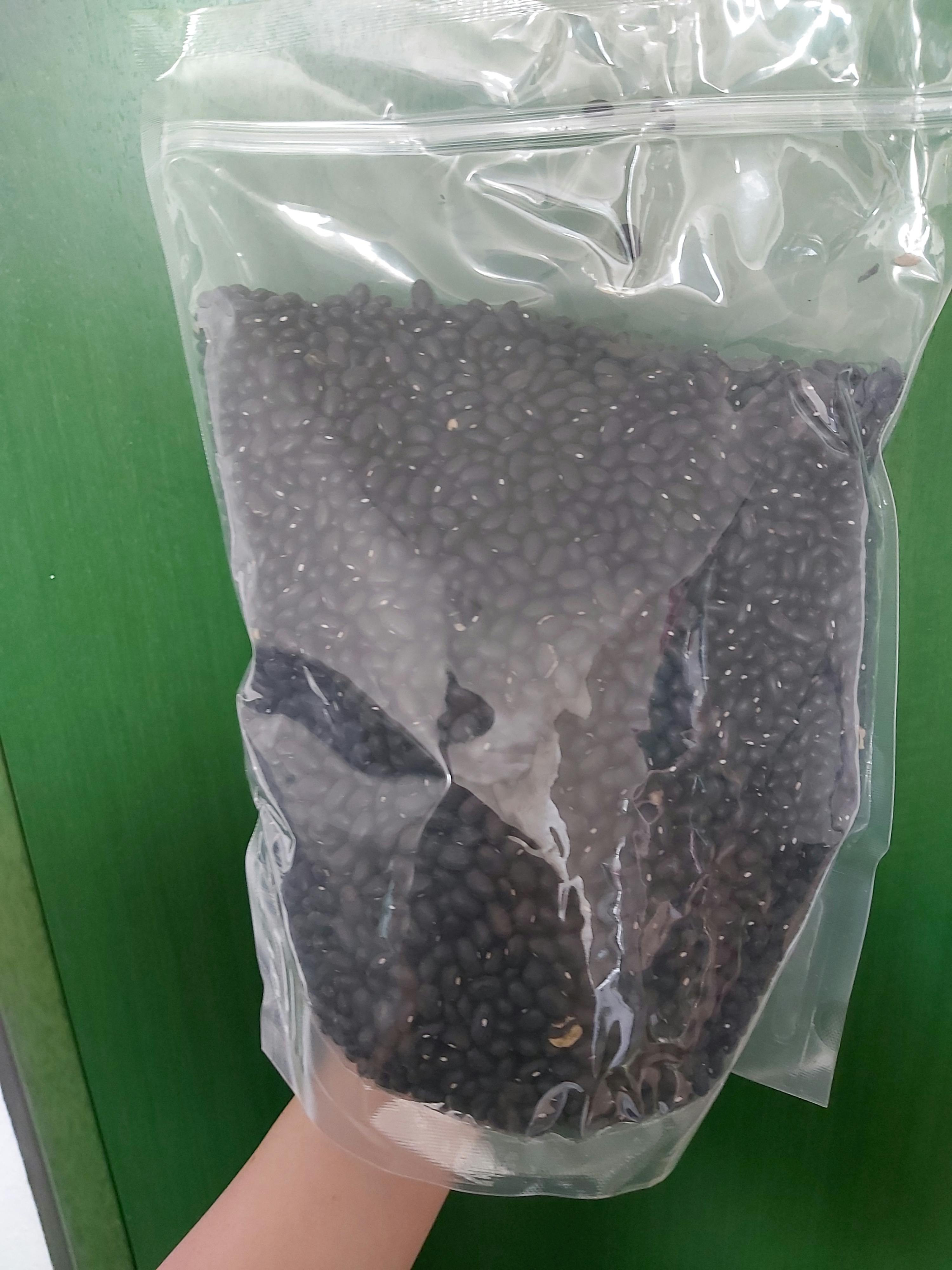 eine Person hält eine Plastiktüte mit schwarzen Bohnen darin