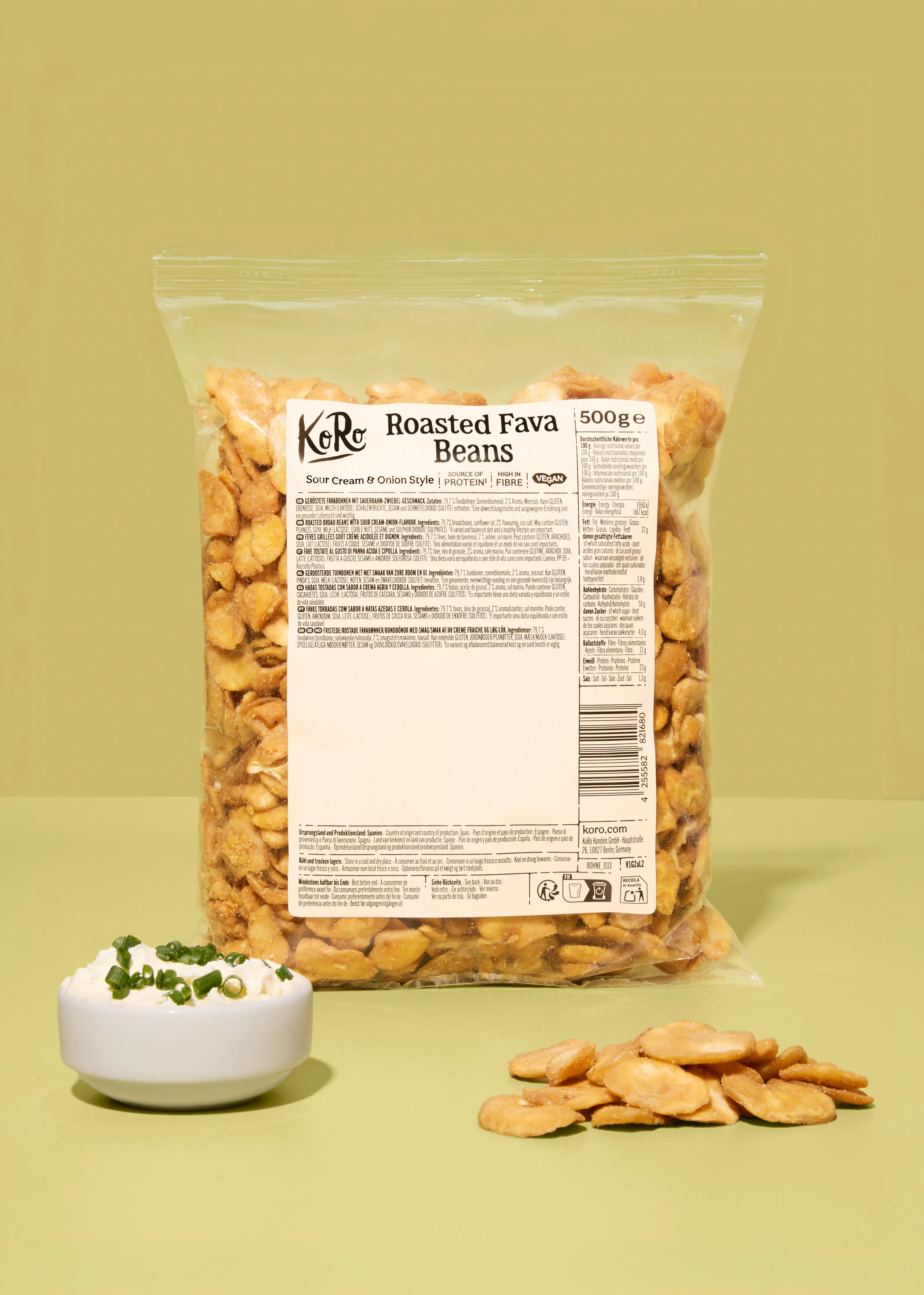 confezione di fave tostate koro al gusto panna acida e cipolla con una ciotolina di salsa guarnita con erba cipollina e alcune fave sparse sul piano di lavoro.