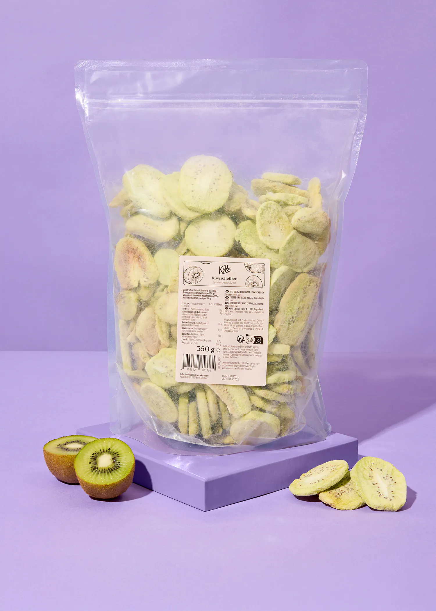 a clear plastic bag of freeze-dried kiwi slices sits on a purple surface, with two fresh kiwi halves and some loose dried slices nearby.
